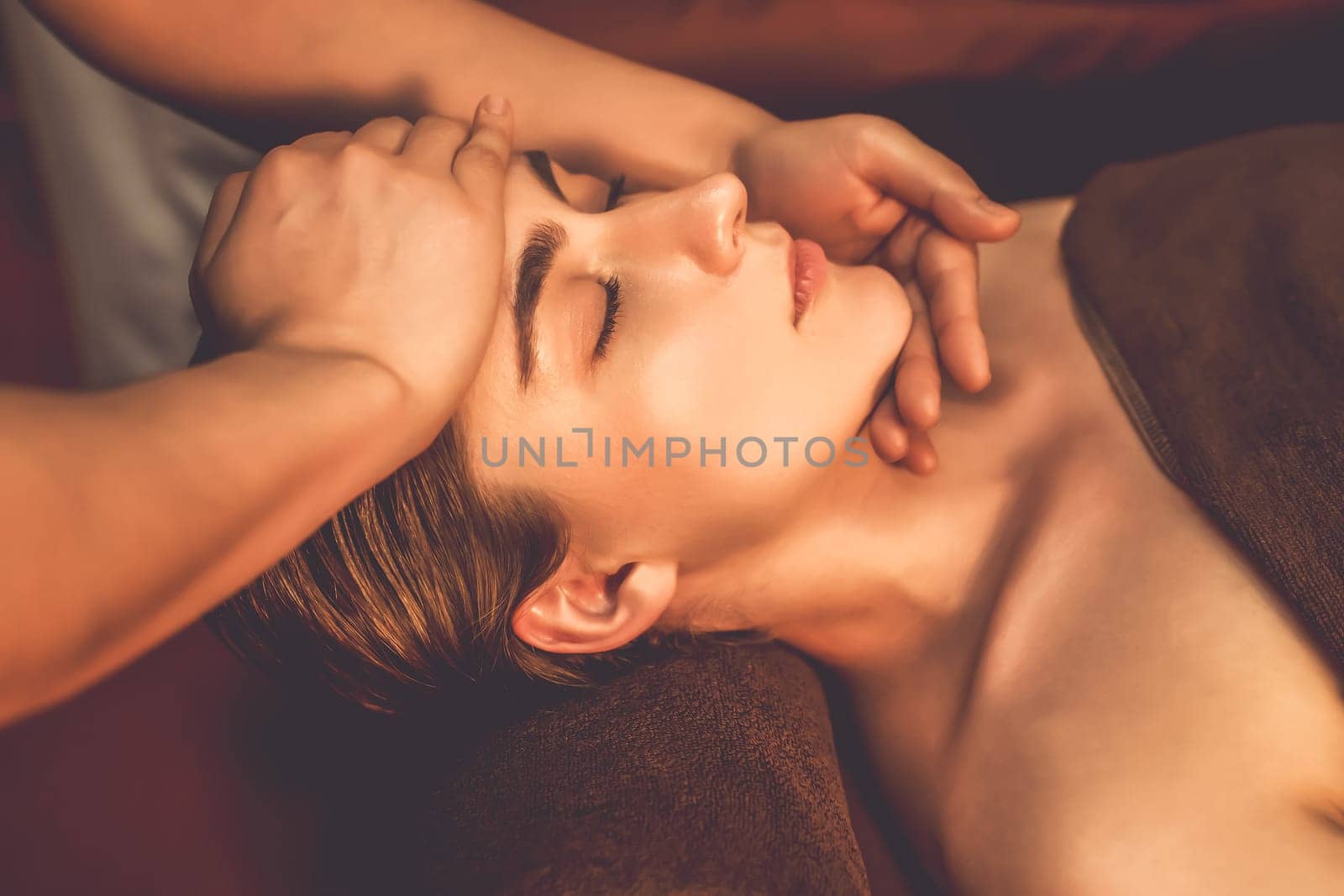 Caucasian woman enjoying relaxing anti-stress head massage and pampering facial beauty skin recreation leisure in warm candle lighting ambient salon spa in luxury resort or hotel. Quiescent