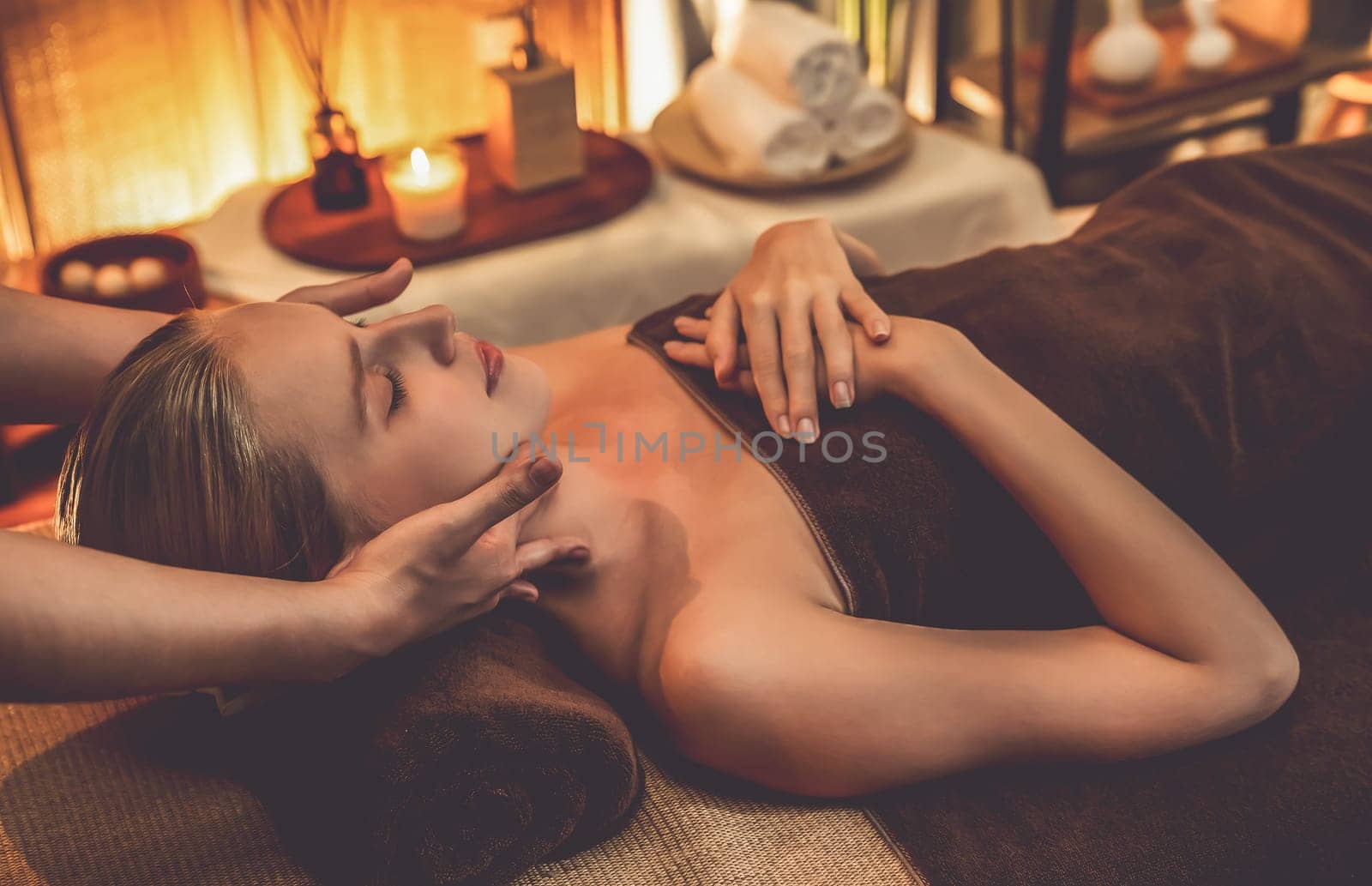 Caucasian woman enjoying relaxing anti-stress head massage and pampering facial beauty skin recreation leisure in warm candle lighting ambient salon spa in luxury resort or hotel. Quiescent