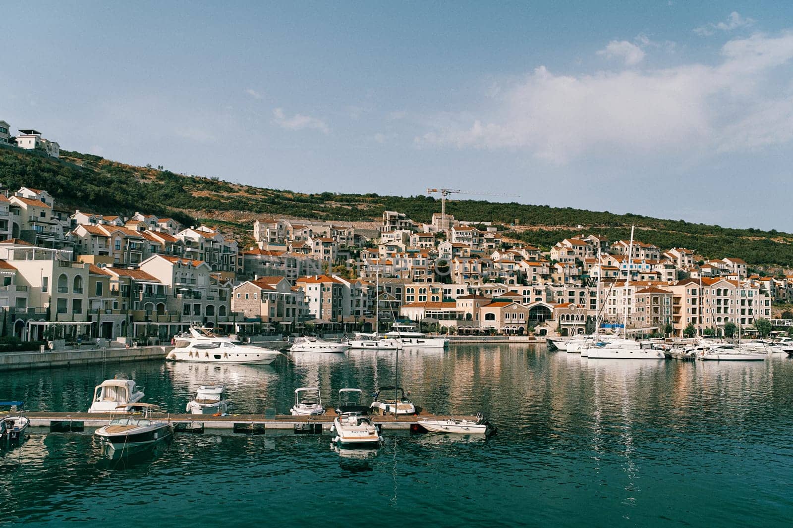 Motor yachts stand along the pier in Lustica Bay against the backdrop of colorful buildings at the foot of the mountains. Montenegro. High quality photo