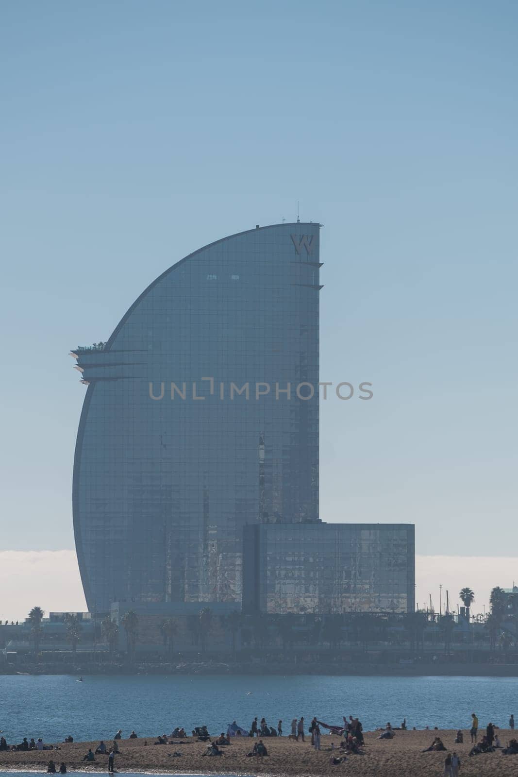 Barcelona, Spain: November 19, 2023: People walk along Barceloneta beach on a sunny day in winter in Barcelona, Catalonia in Spain in winter 2023.