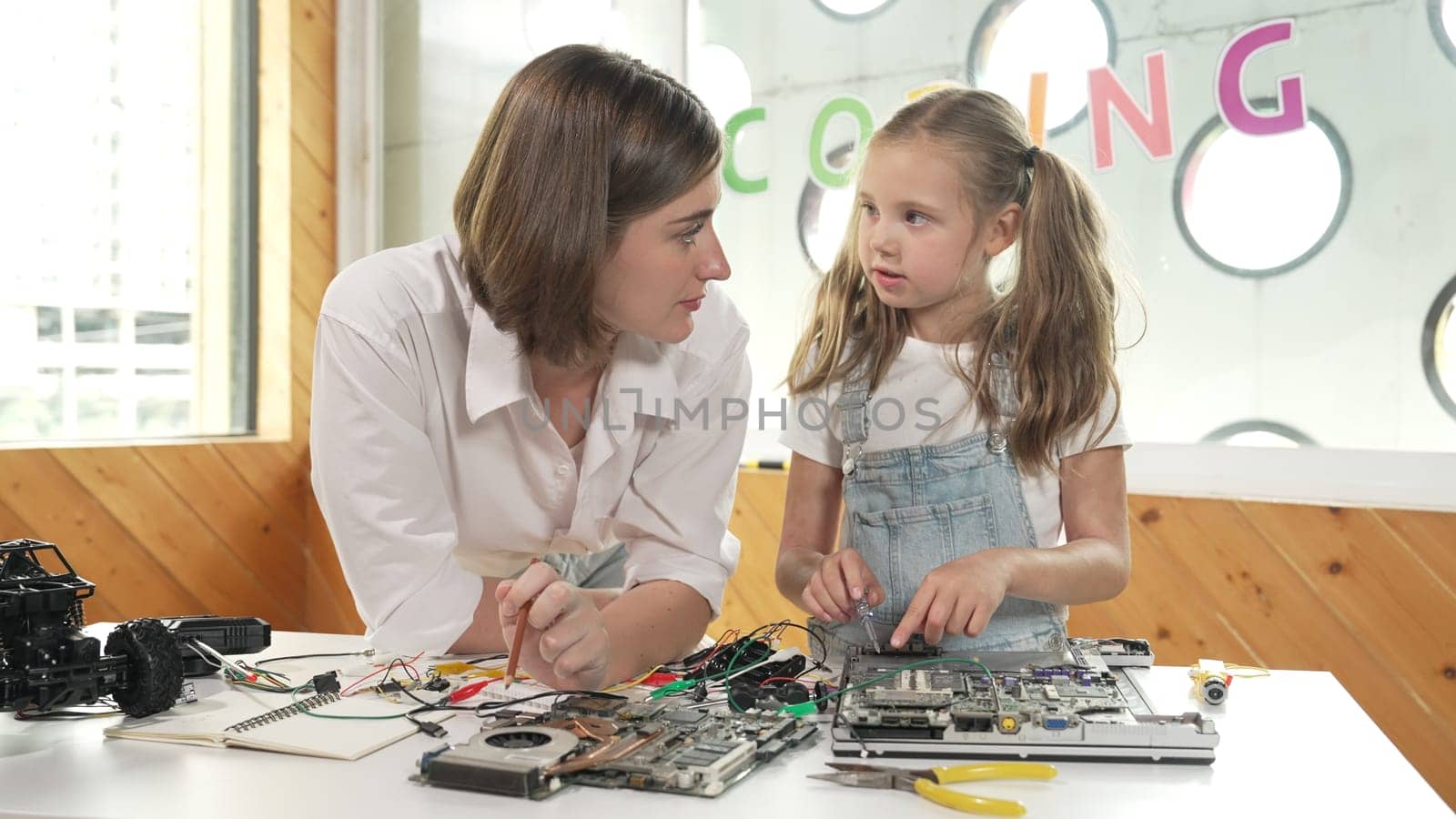 Young smart caucasian teacher teaching students about part of electronic board. Expert girl learn about digital electrical tool and fixing motherboard at table with chips and wires placed. Erudition.