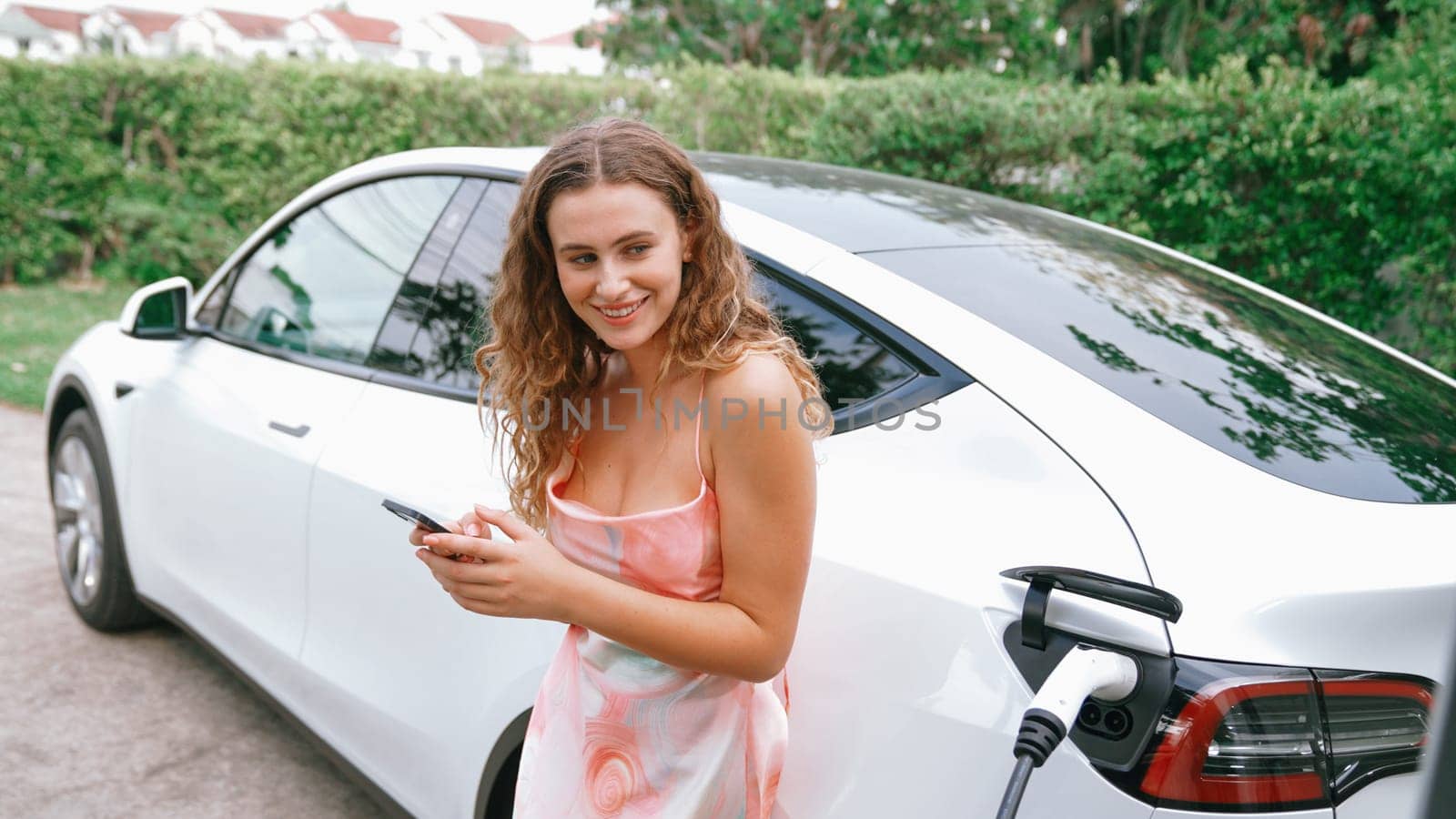 Young woman use smartphone to pay for electricity for EV car. Synchronos by biancoblue