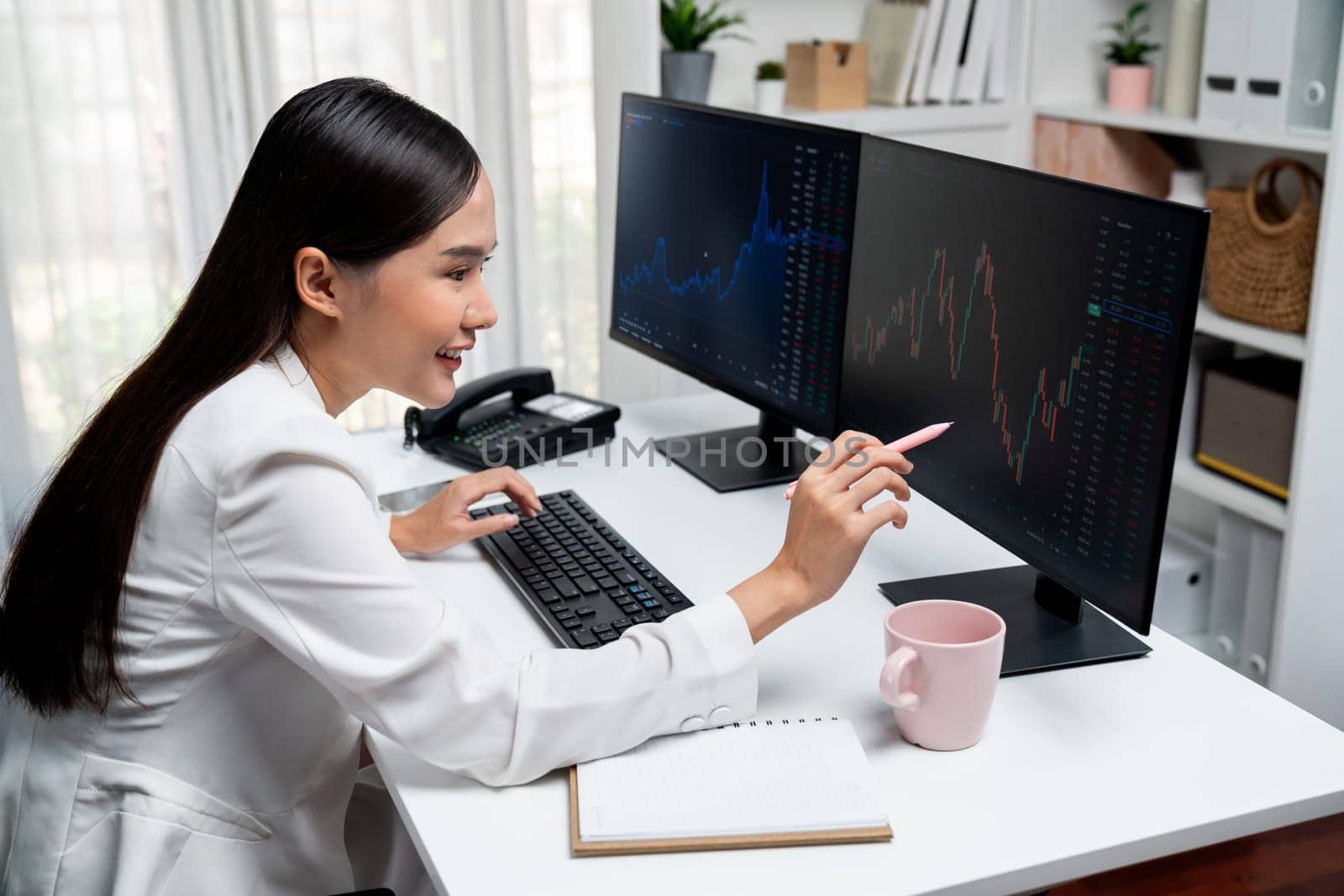 Young beautiful Asian businesswoman looking on pc to analyze profitable of exchange stock market graph at modern office. Concept of investing high profit in wealth security in finance. Stratagem.