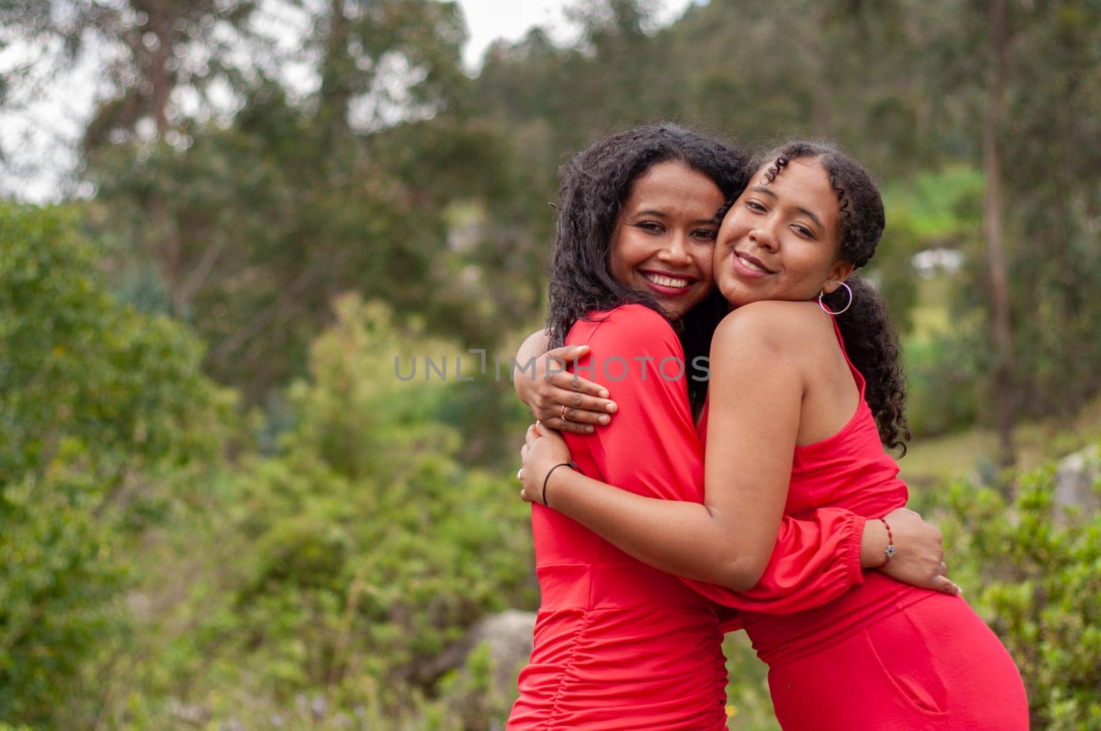 copyspace of two friends giving each other a happily sincere hug while looking at the camera in red dresses. hug day. by Raulmartin