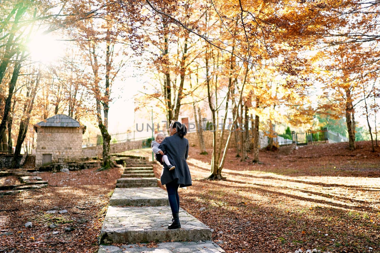 Mom with a little girl in her arms walks along a paved path with steps in an autumn park. High quality photo