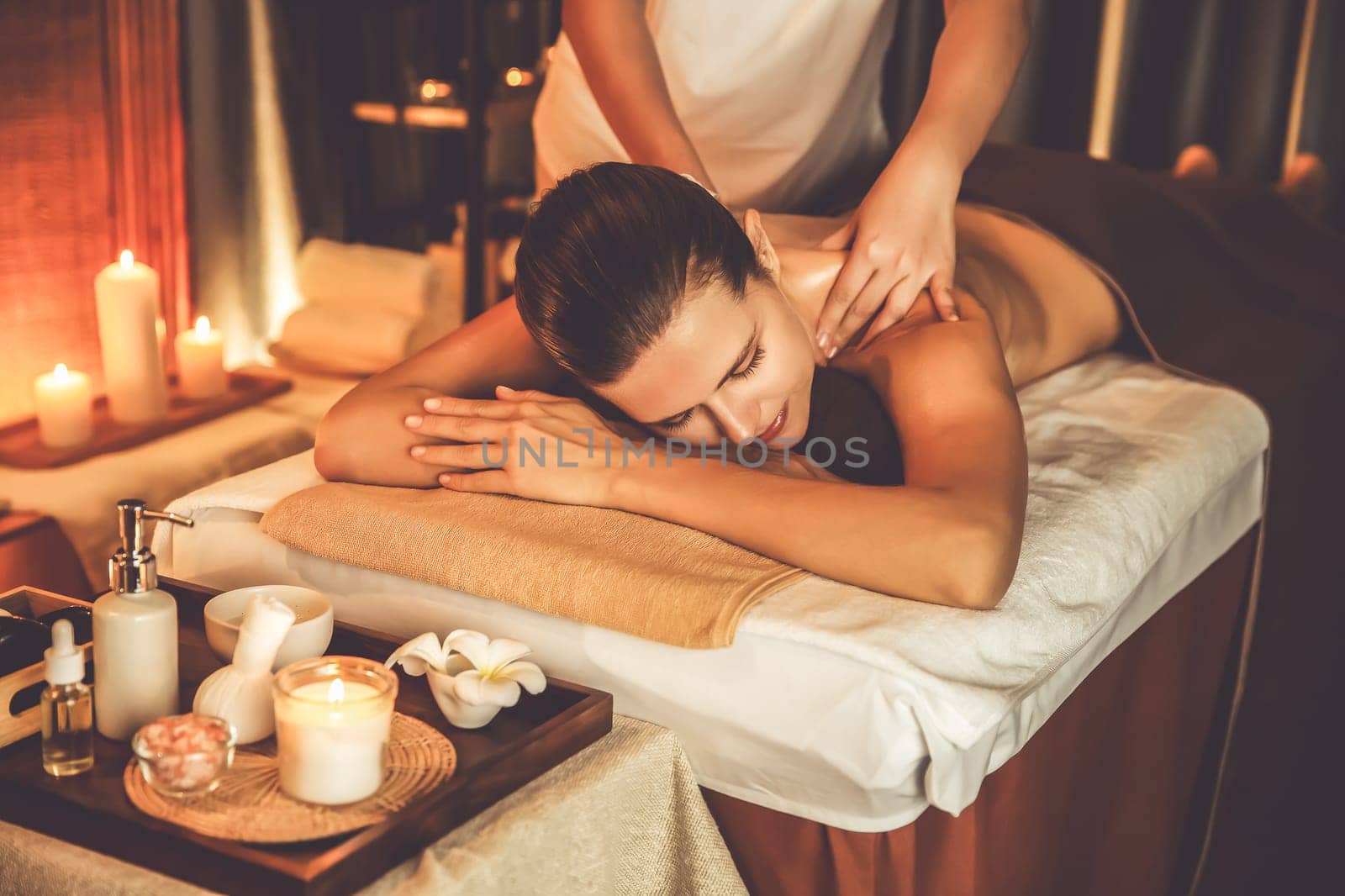 Caucasian woman customer enjoying relaxing anti-stress spa massage and pampering with beauty skin recreation leisure in warm candle lighting ambient salon spa at luxury resort or hotel. Quiescent