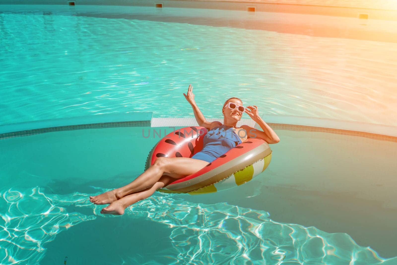 Happy woman in a swimsuit and sunglasses floating on an inflatable ring in the form of a watermelon, in the pool during summer holidays and vacations. Summer concept. by Matiunina