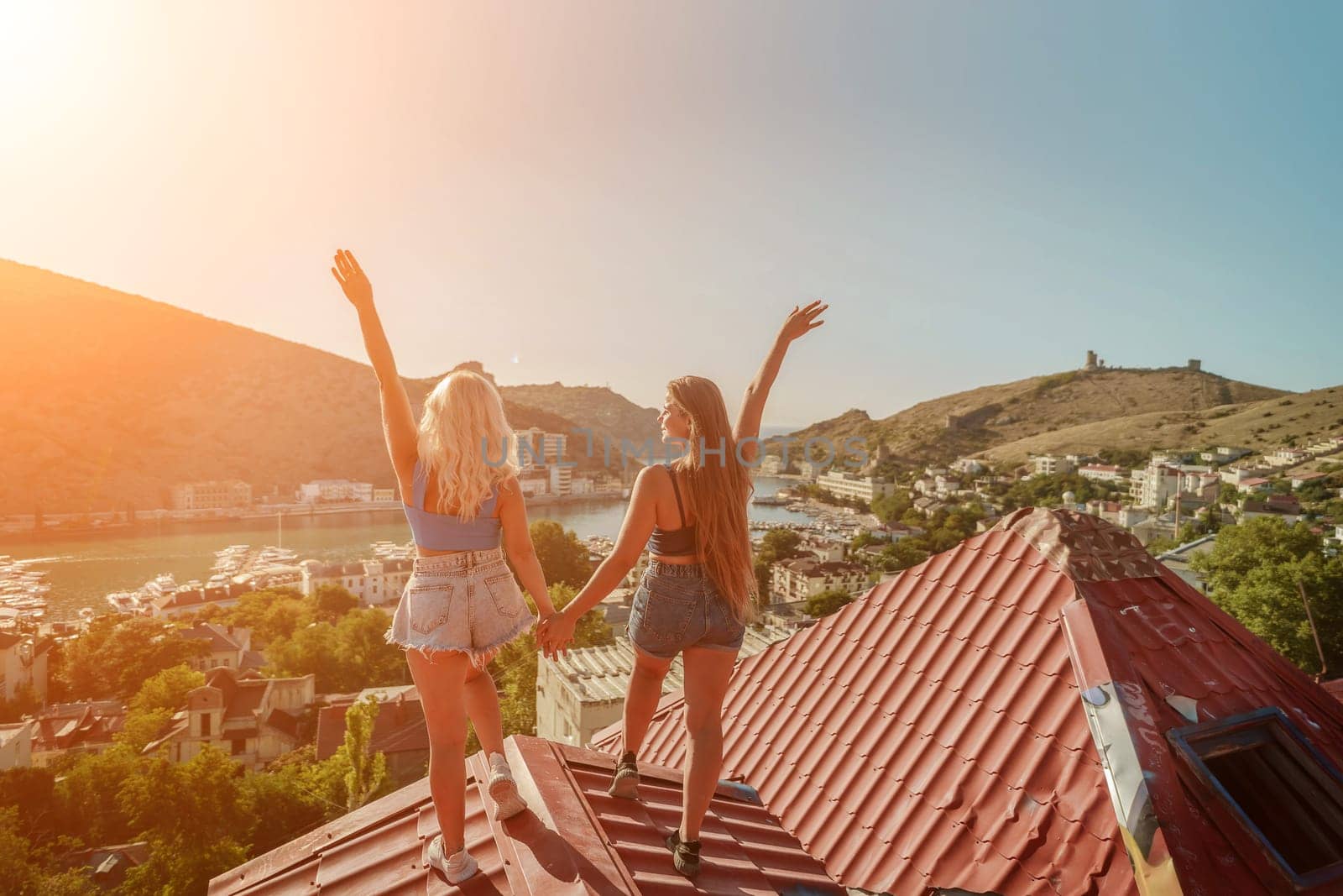 women standing on rooftop, enjoys town view and sea mountains. Peaceful rooftop relaxation. Below her, there is a town with several boats visible in the water. Rooftop vantage point. by Matiunina