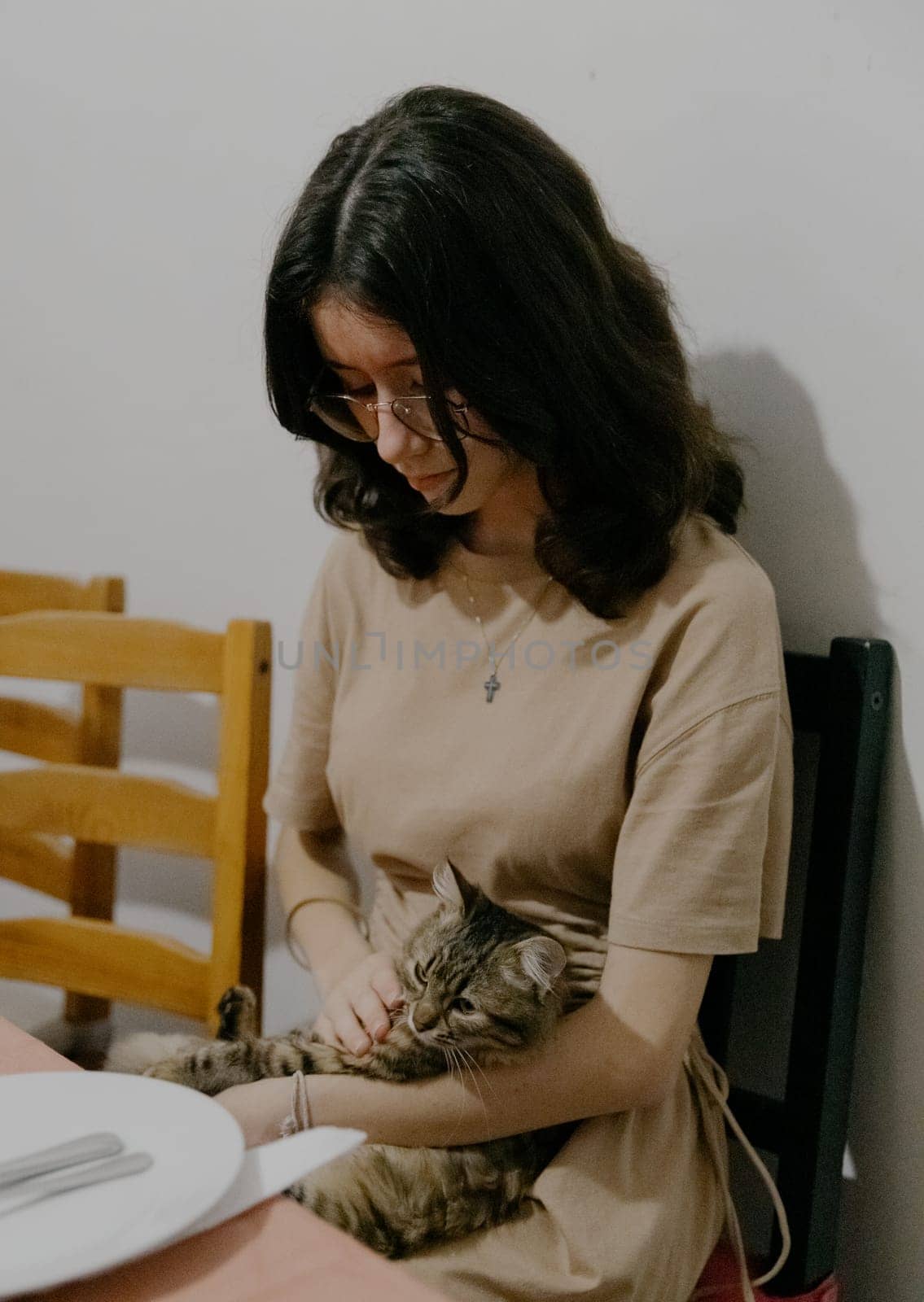 A teenage girl with a cat in her arms sits at the table. by Nataliya