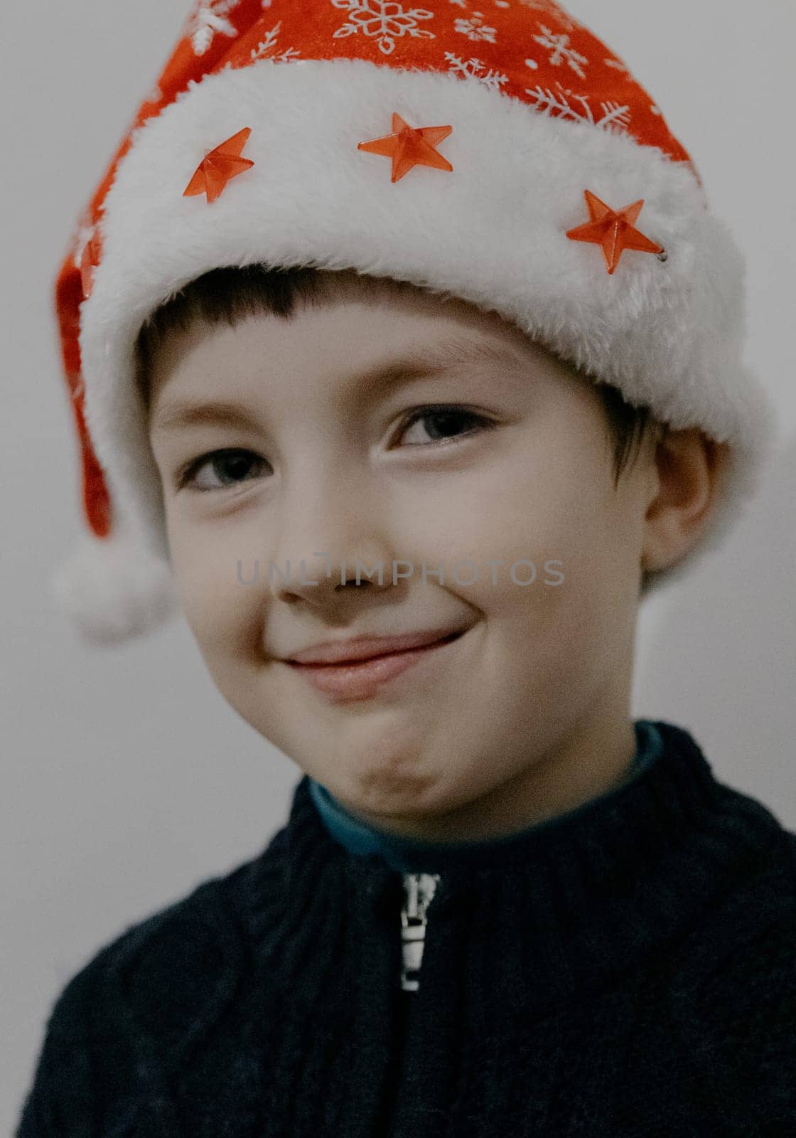 Portrait of one small beautiful Caucasian boy in a Santa Claus hat with a sweet smile and a look at the camera, close-up side view.