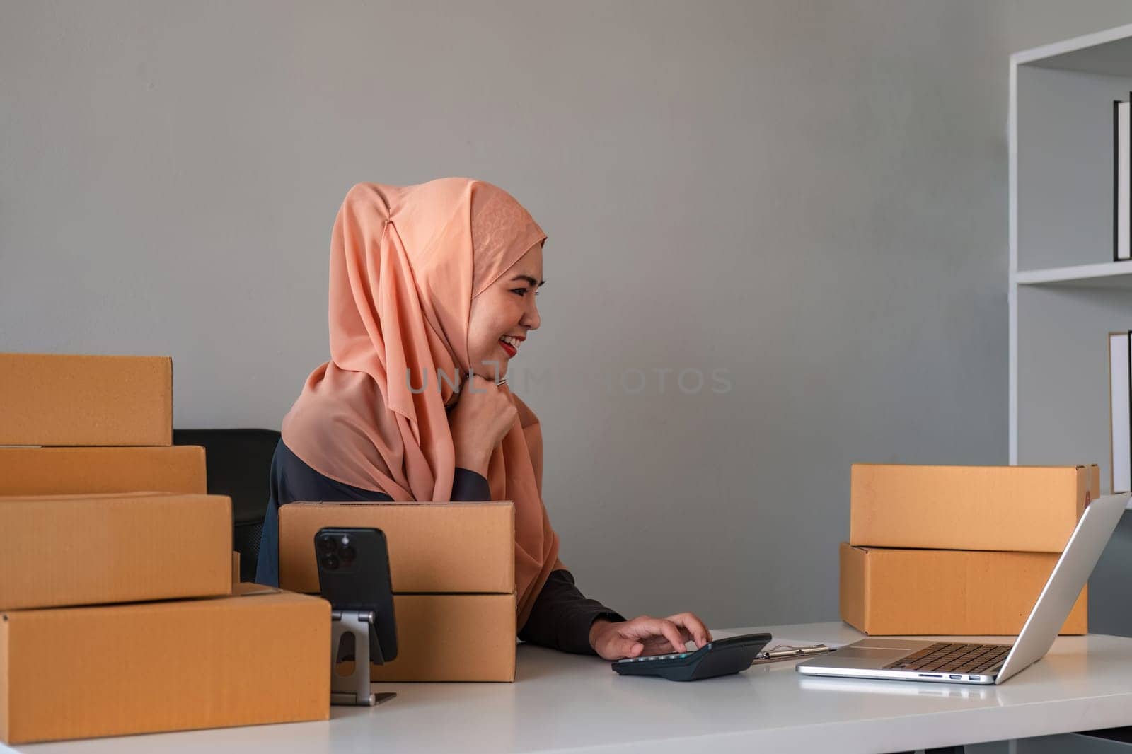 Asian Muslim businesswoman checks stock orders and saves them on her home office laptop. small business owner Shipping in online markets The concept of freedom in life.