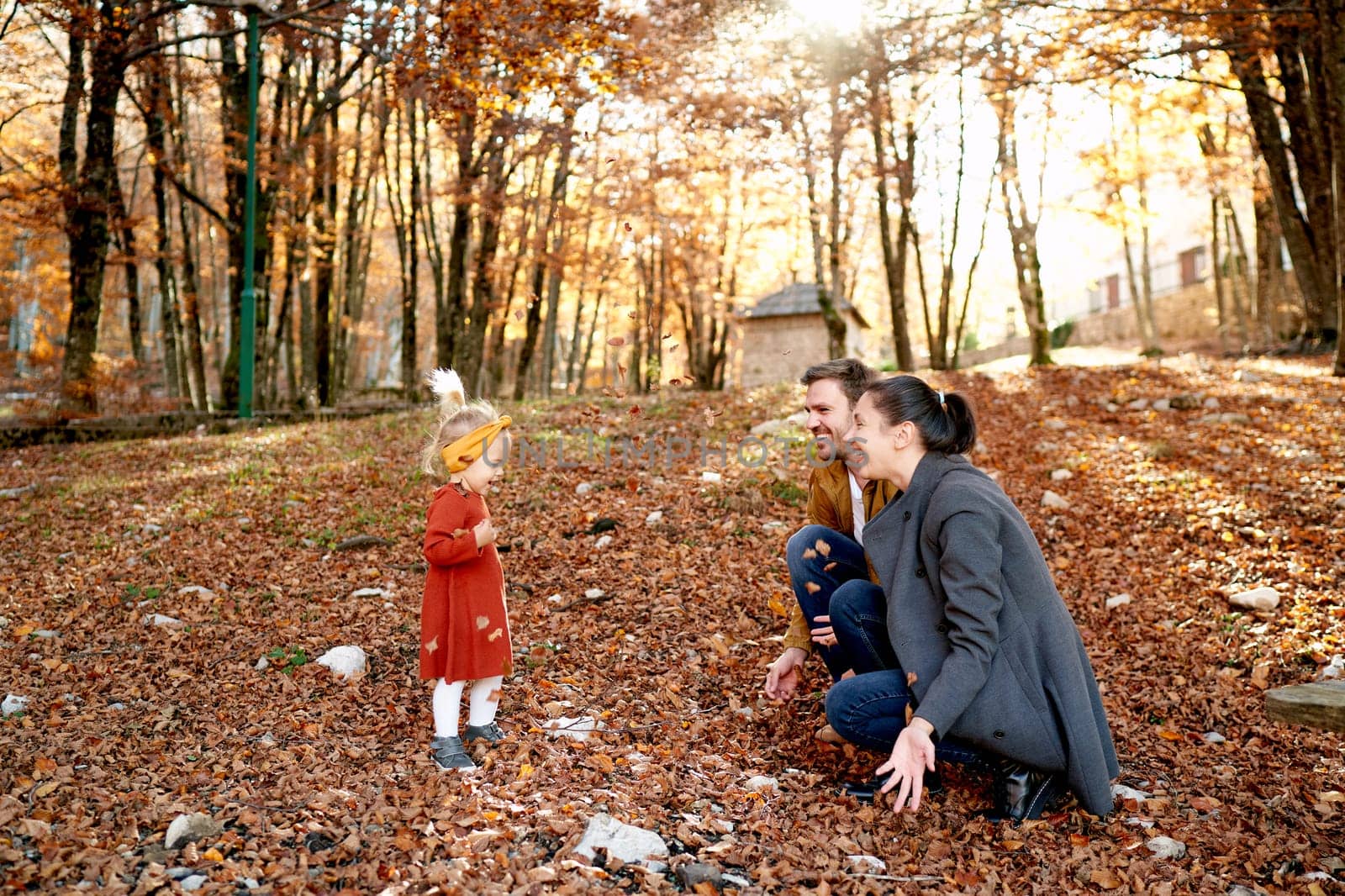Little girl stands in front of smiling mom and dad squatting in the forest. High quality photo