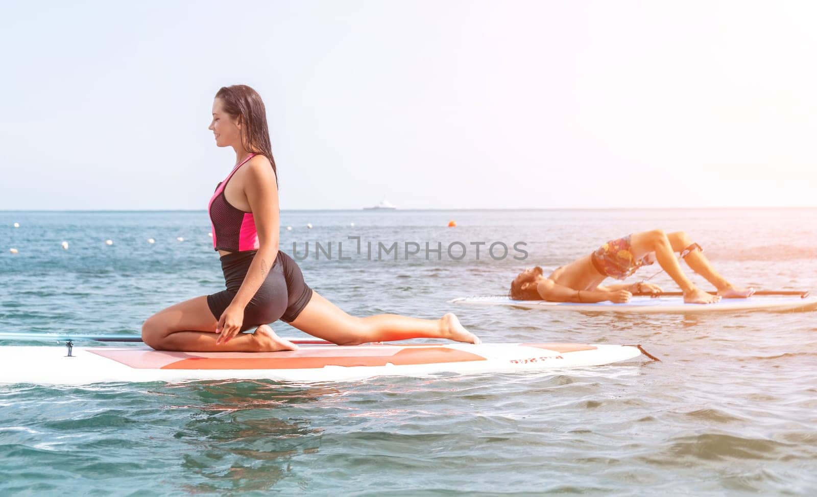 Woman sup yoga. Happy young sporty woman practising yoga pilates on paddle sup surfboard. Female stretching doing workout on sea water. Modern individual female outdoor summer sport activity