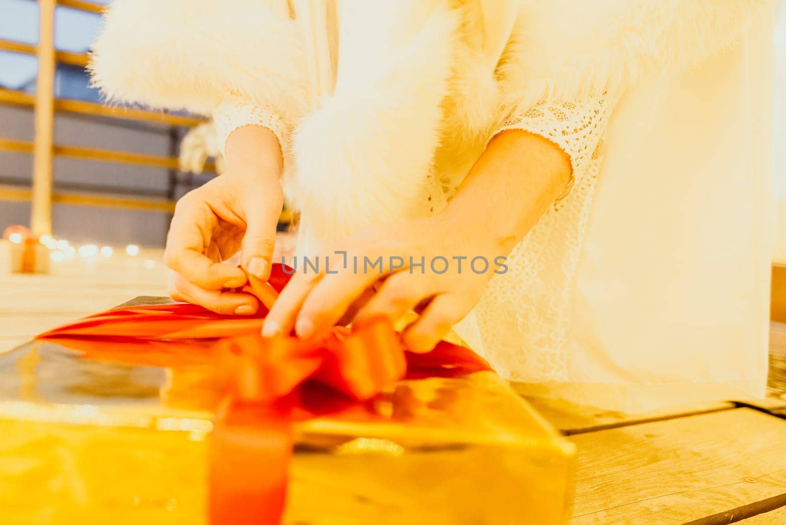 A woman in a white dress is holding a gold box with a red ribbon. She is wearing a crown on her head. The woman appears to be opening the gift box. by panophotograph