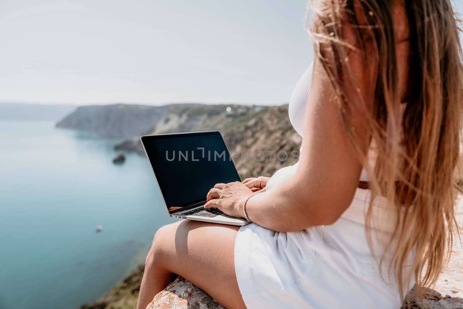 Digital nomad, Business woman working on laptop by the sea. Pretty lady typing on computer by the sea at sunset, makes a business transaction online from a distance. Freelance, remote work on vacation by panophotograph