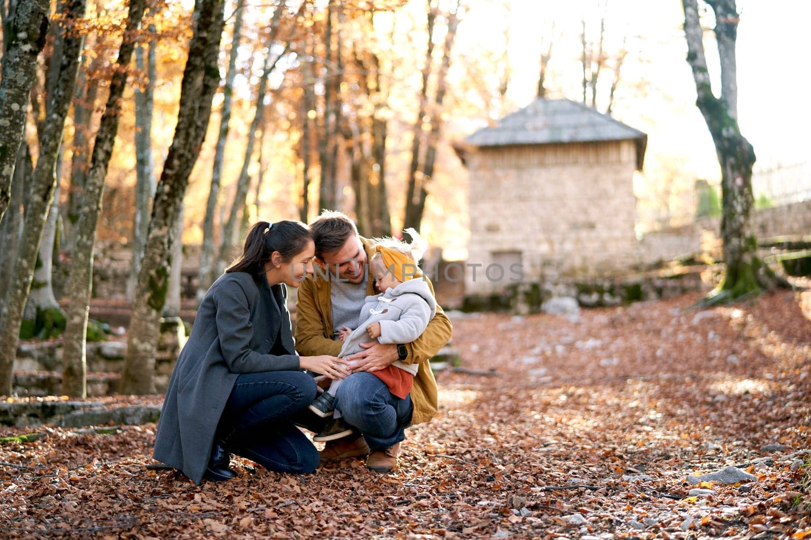 Mom squats and looks at a little girl on her dad lap in an autumn park. High quality photo