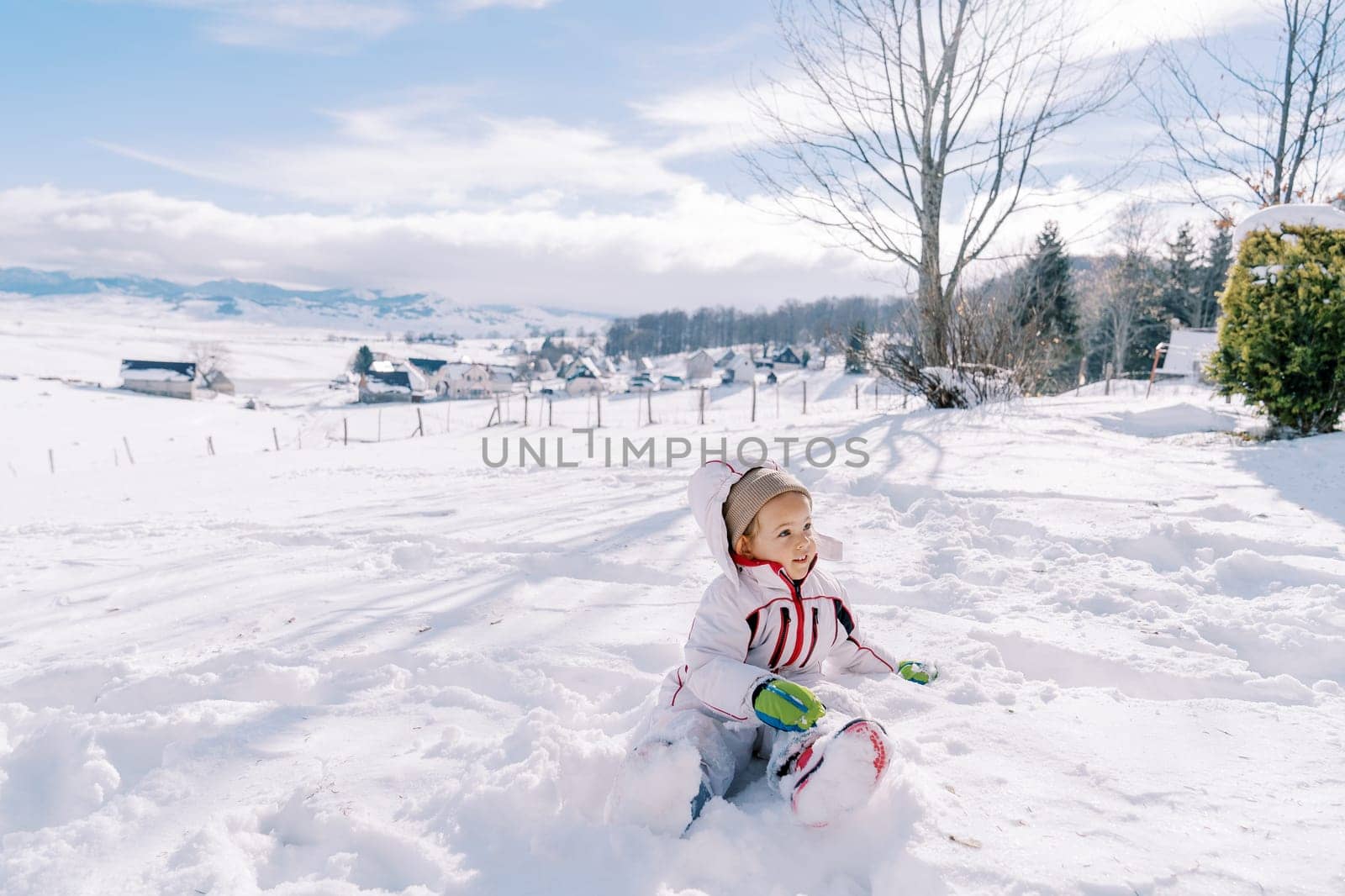 Little girl sits half-turned in a snowdrift and looks away. High quality photo