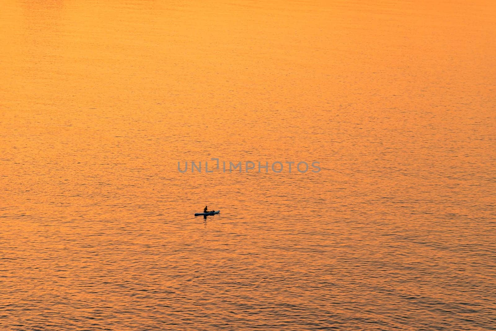 Adventurous people on a stand up paddle board is paddling during a bright and vibrant sunrise