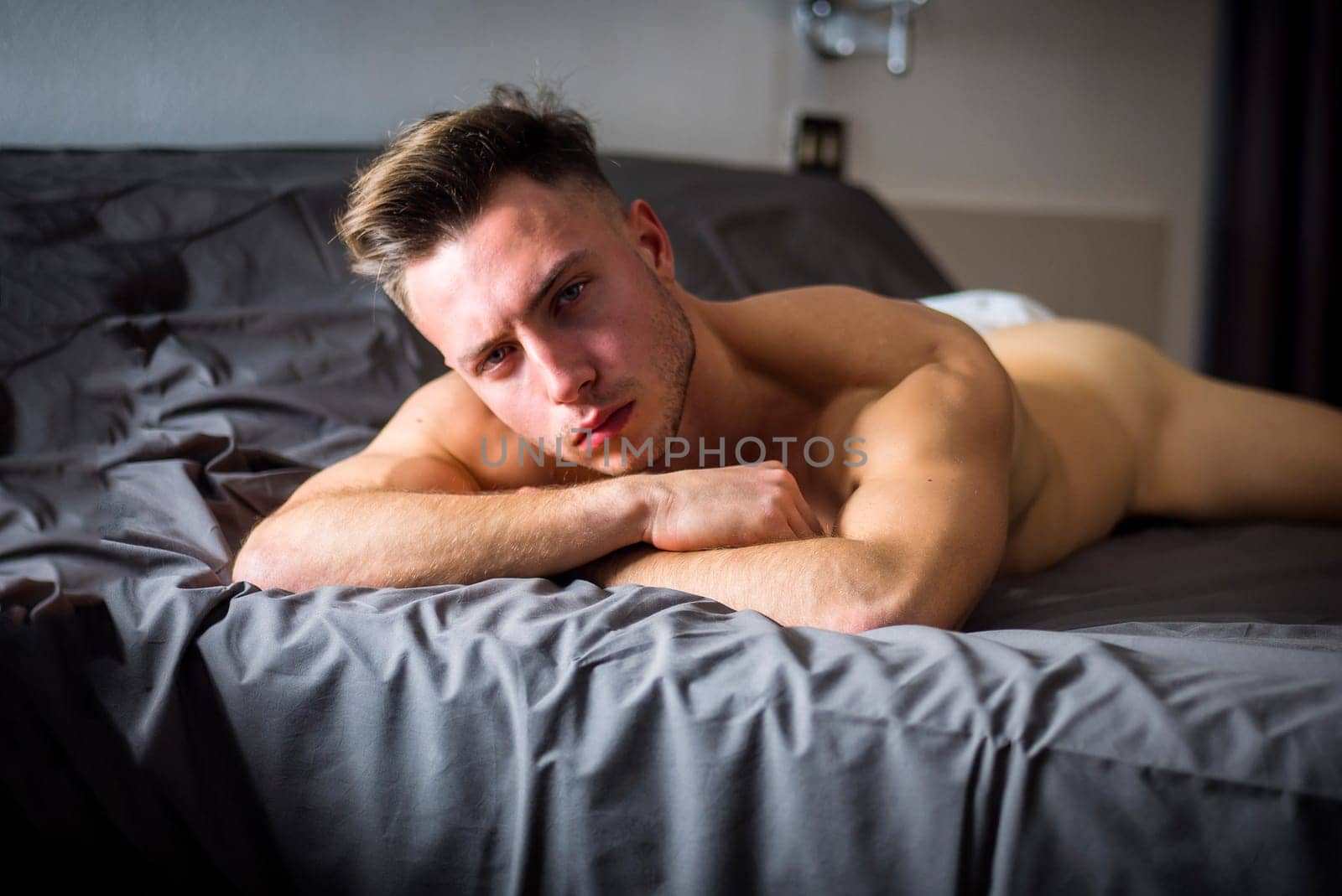 Totally naked sexy young man with muscular body on bed looking at camera