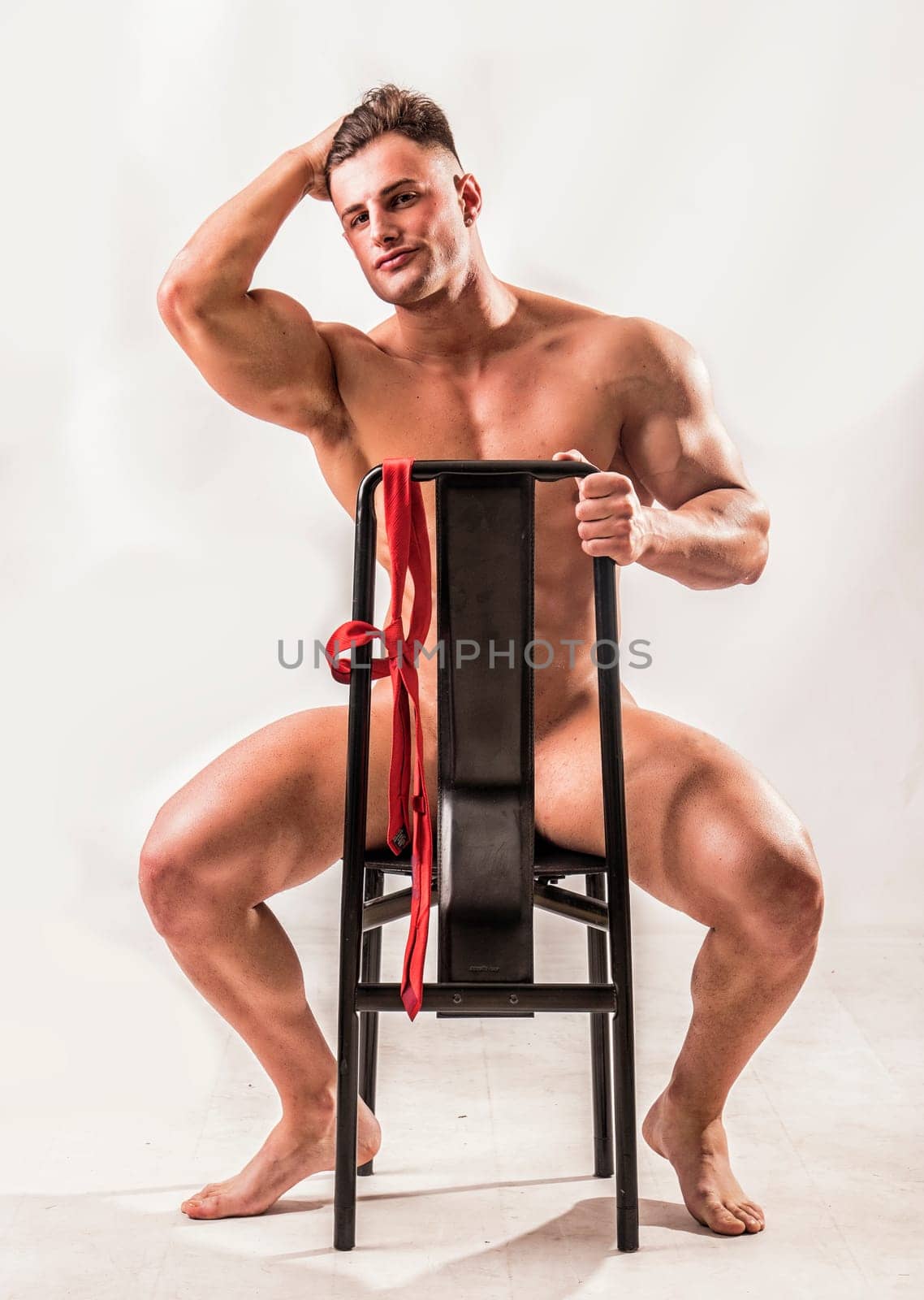 Muscular bodybuilder sitting on chair, totally naked, looking at camera