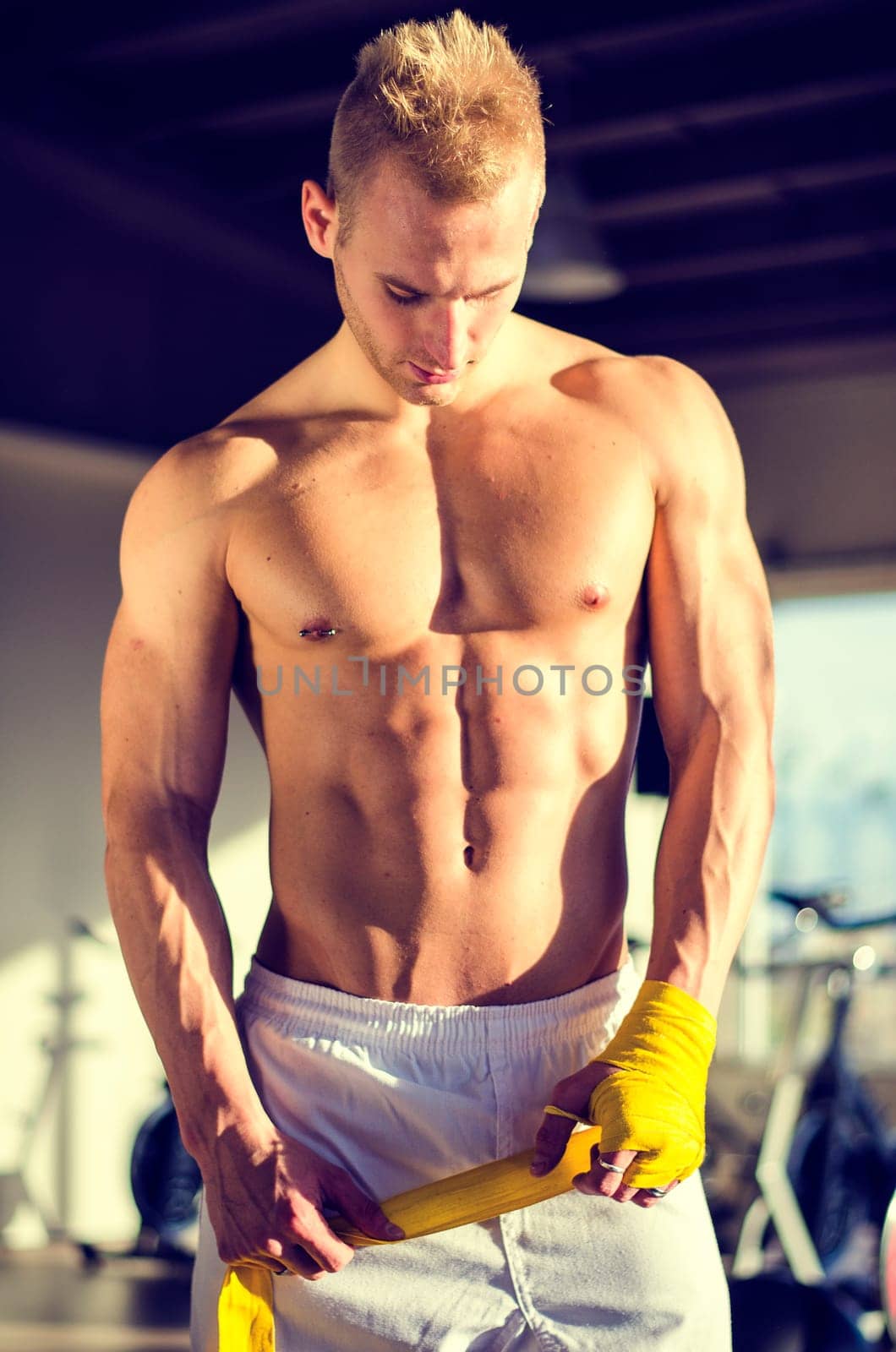 Muscular young man wrapping bandage around his hands for boxing