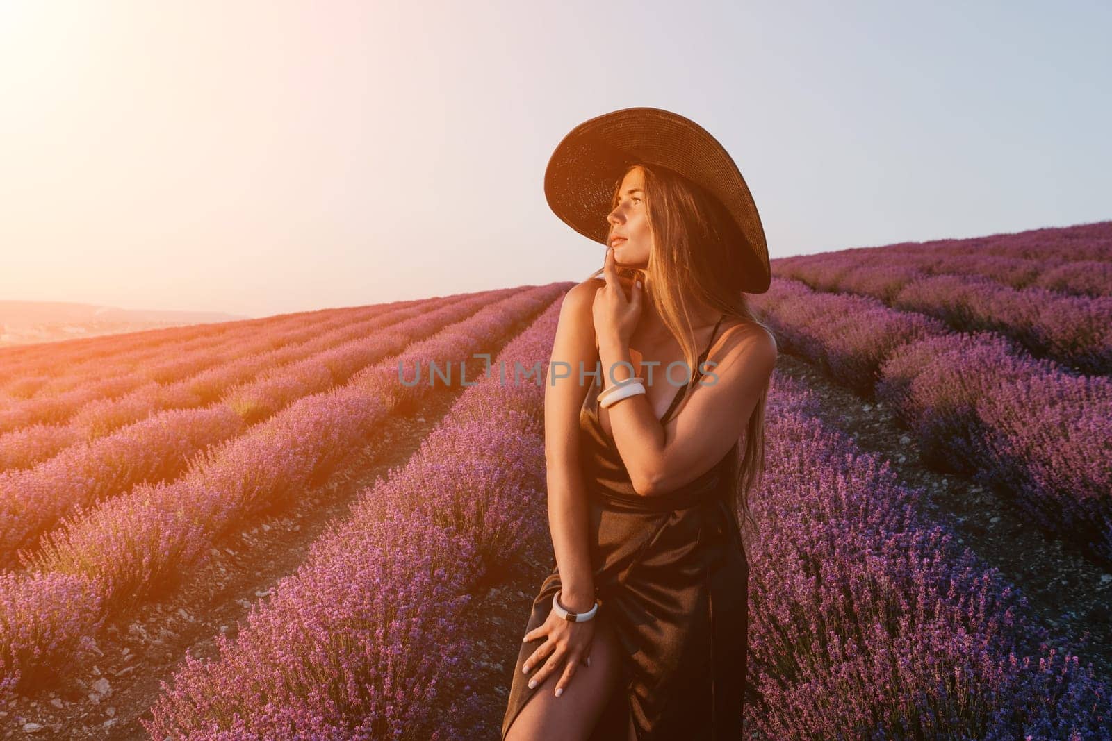 Close up portrait of young beautiful woman in a white dress and a hat is walking in the lavender field and smelling lavender bouquet.