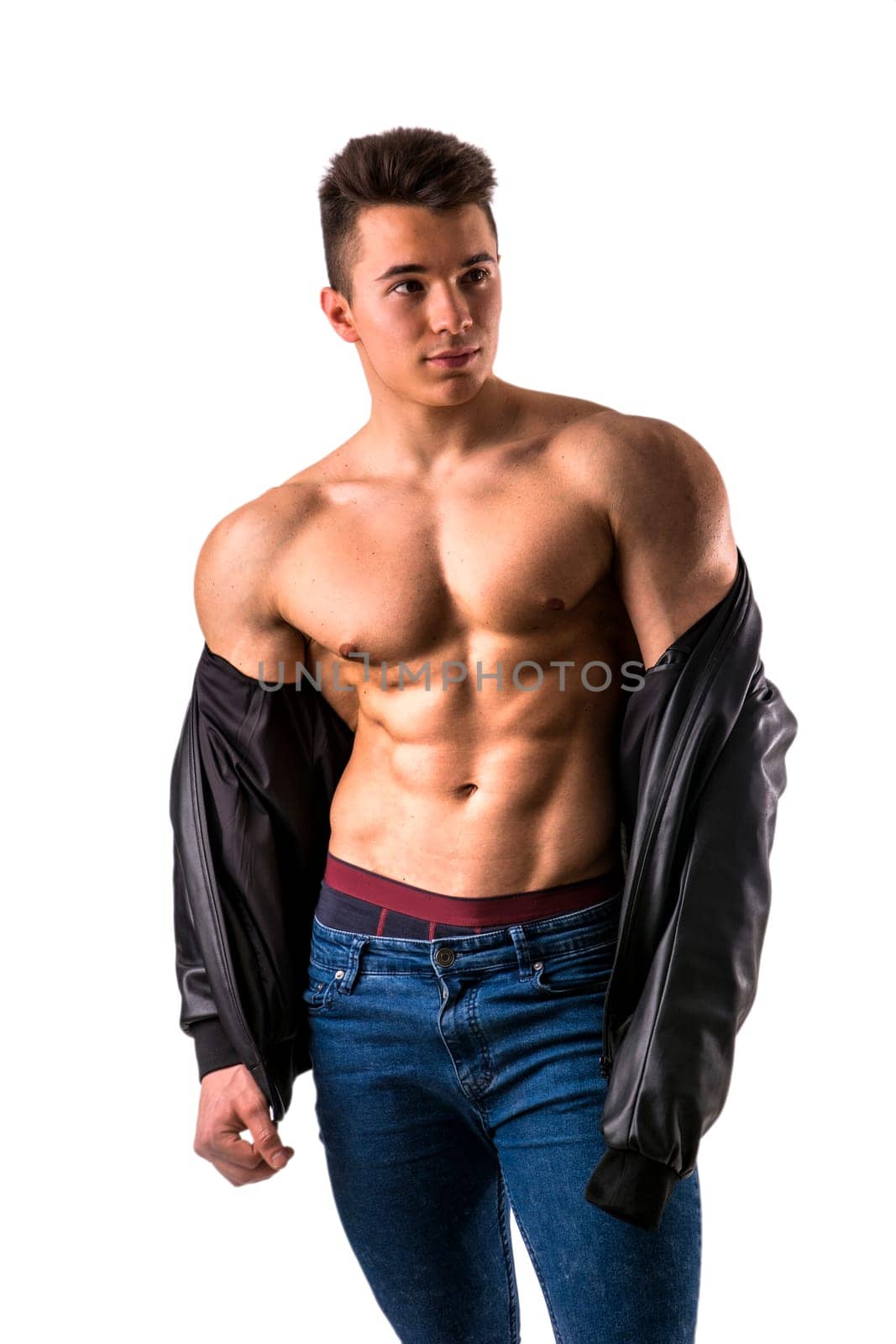 Handsome young muscular man shirtless wearing jeans, taking off leather jacket on naked muscle torso, isolated on white background in studio shot