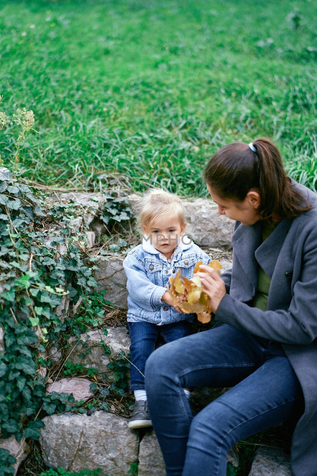Mom with a little girl are sitting on the steps in the park and holding a yellow branch in their hands. High quality photo