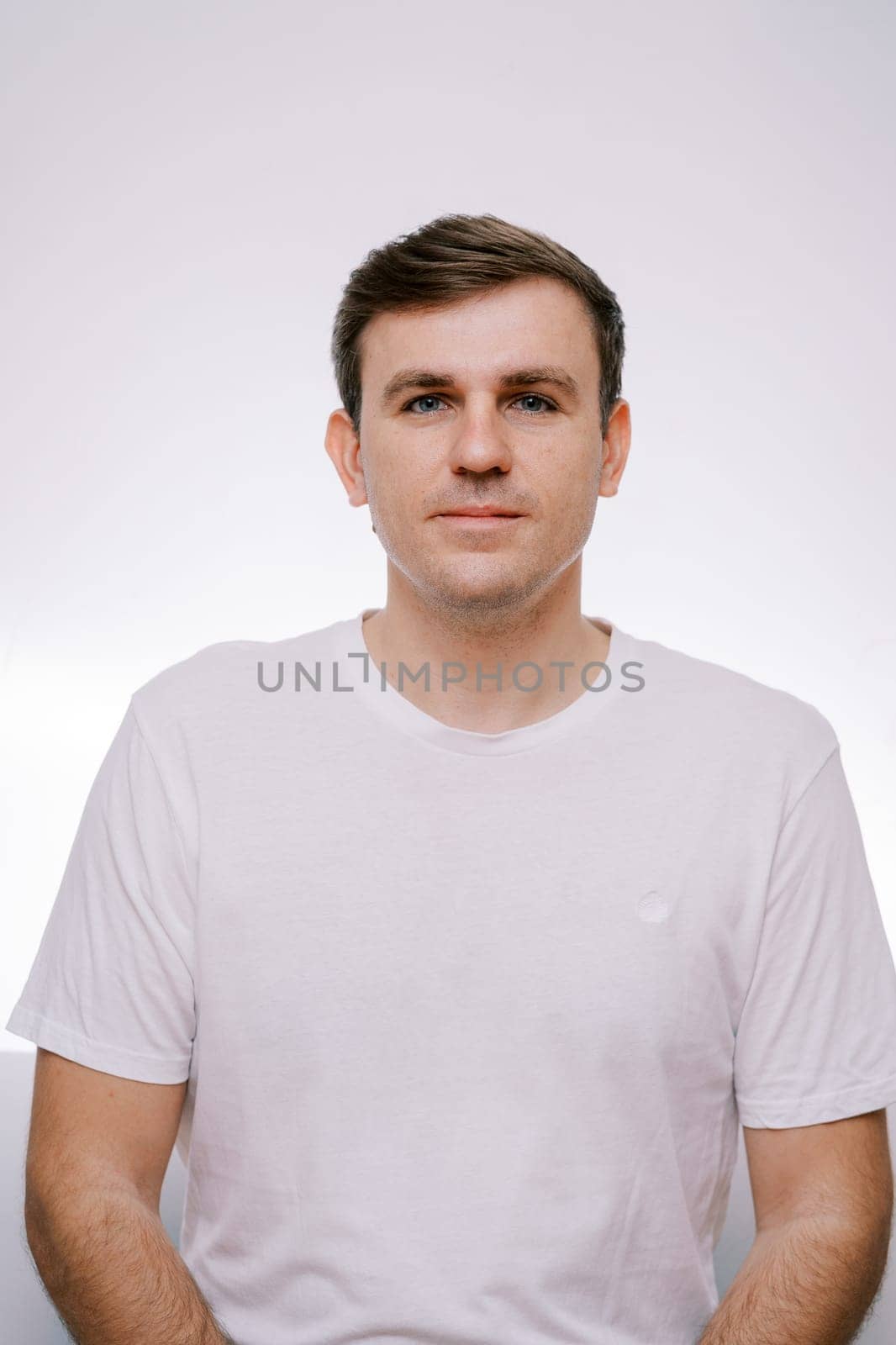 Young serious man in a white T-shirt on a gray background. Portrait by Nadtochiy