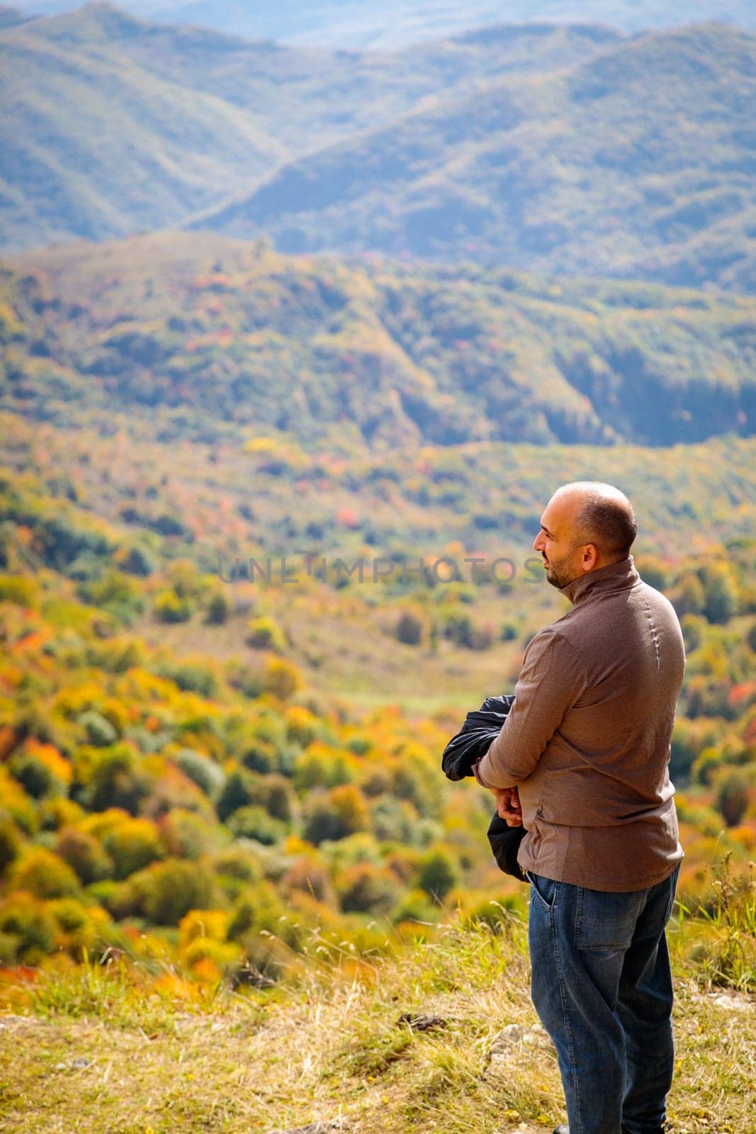 A serene moment captured as a man looks out in awe at the spectacular mountain landscape from a sacred outlook point, with the vast valley below creating a breathtaking scene.
