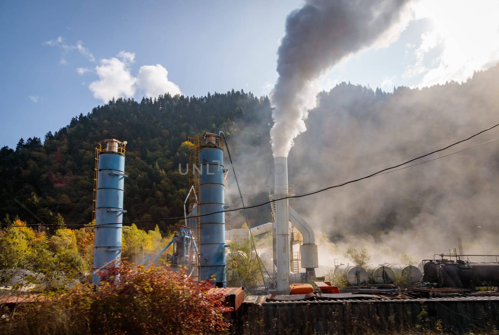 Industrial landscape with smoking factory chimneys on the background of mountainous terrain, reflecting the impact of human activity on the environment