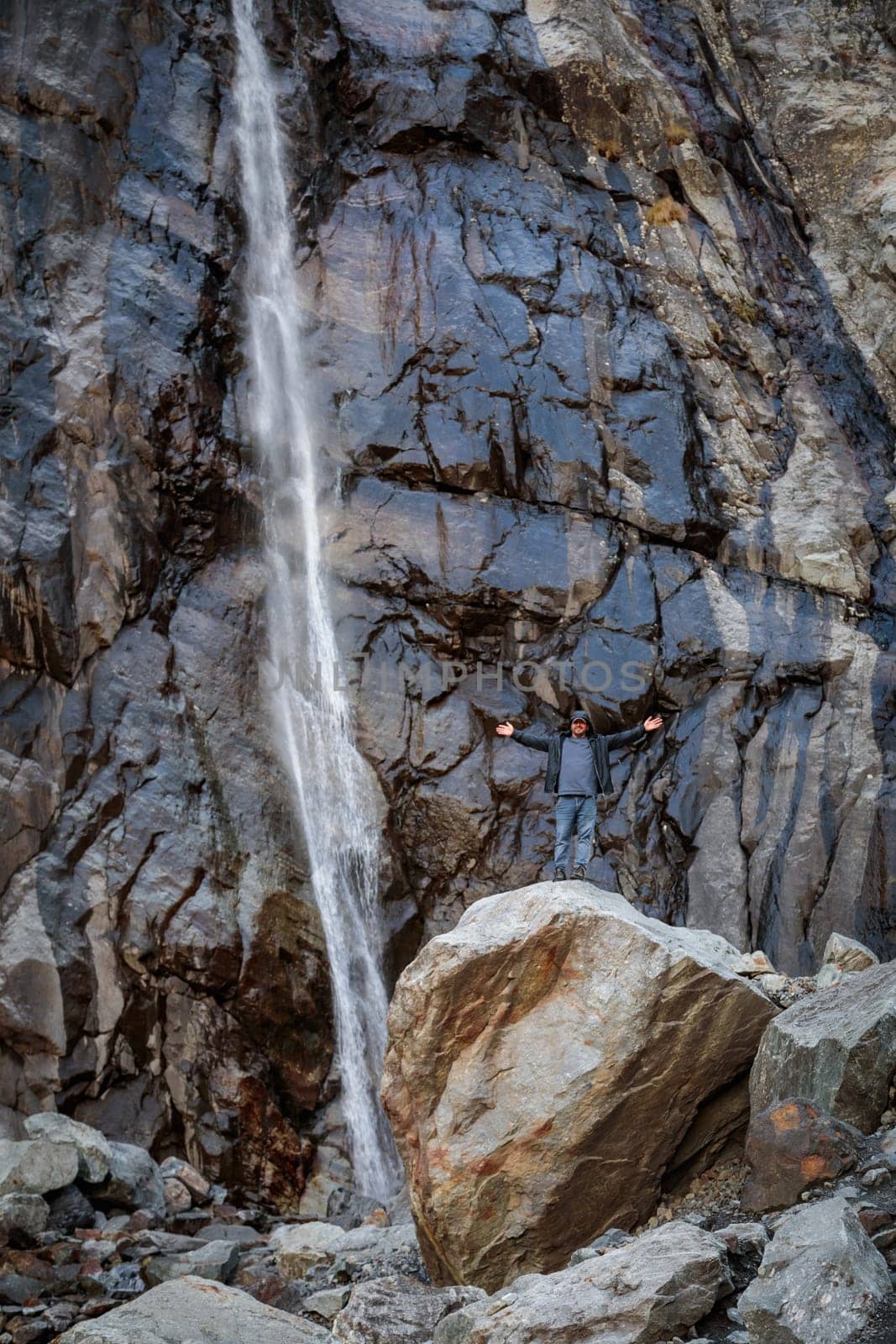 A man contemplates the majesty of a mountain waterfall, reflected in a quiet union with nature