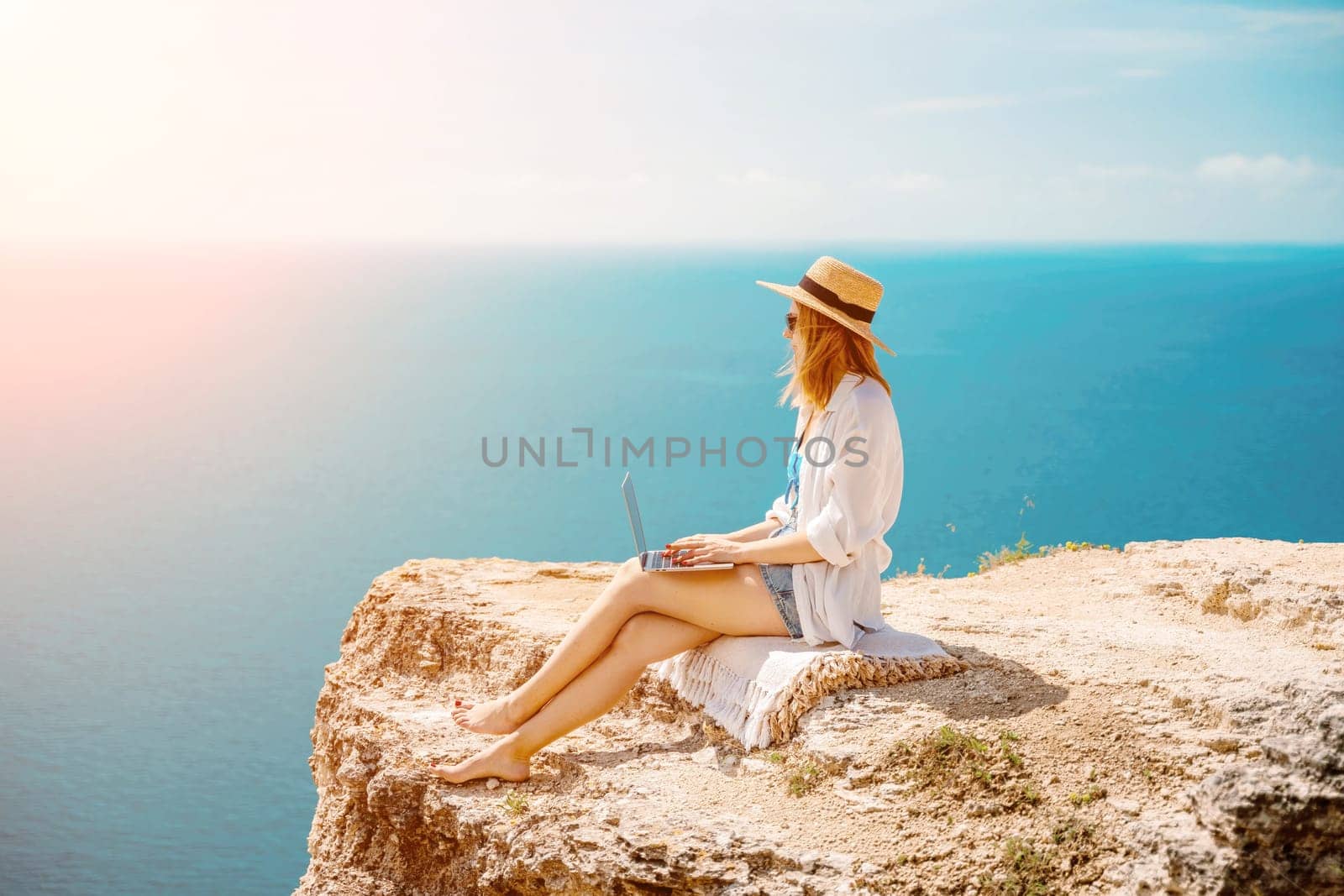 Freelance woman working on a laptop by the sea, typing away on the keyboard while enjoying the beautiful view, highlighting the idea of remote work