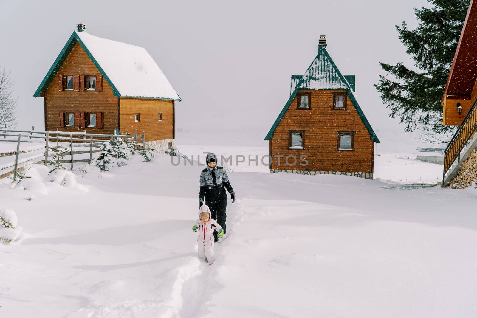 Mom and little girl walk through snowdrifts near wooden houses in the village. High quality photo