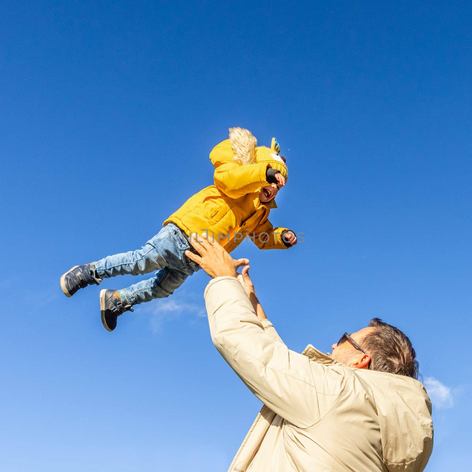 More, more,...dad, that's fun. Happy young father throws his cute little baby boy up in the air. Father's Day, Father and his son baby boy playing and hugging outdoors in nature in fall. by kasto