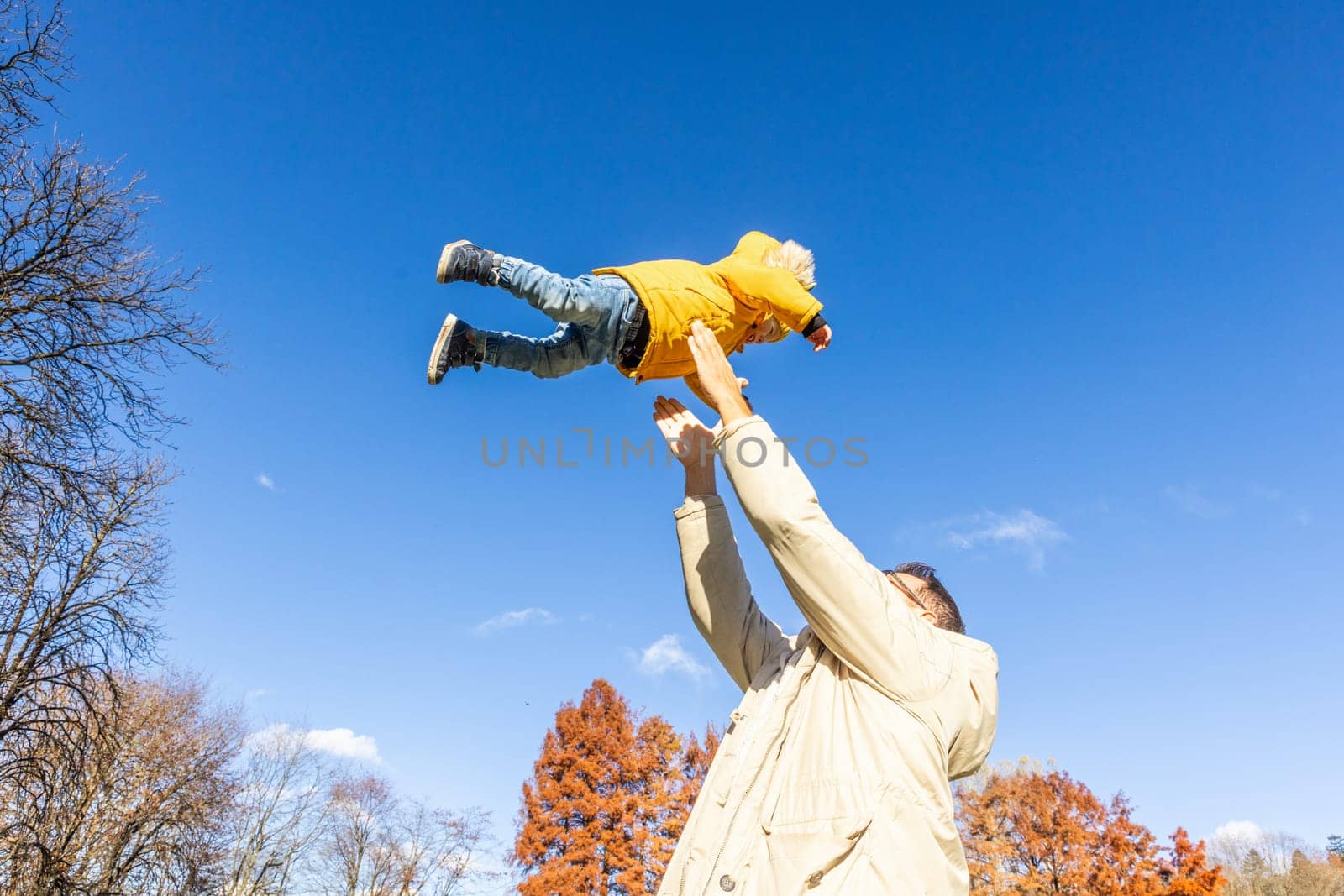 More, more,...dad, that's fun. Happy young father throws his cute little baby boy up in the air. Father's Day, Father and his son baby boy playing and hugging outdoors in nature in fall. by kasto