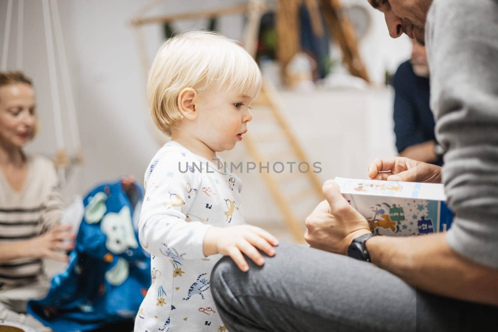 Cute little blond Caucasian toddler unpacking Christmas or Birthday present. Adorable small infant baby boy opening gift.