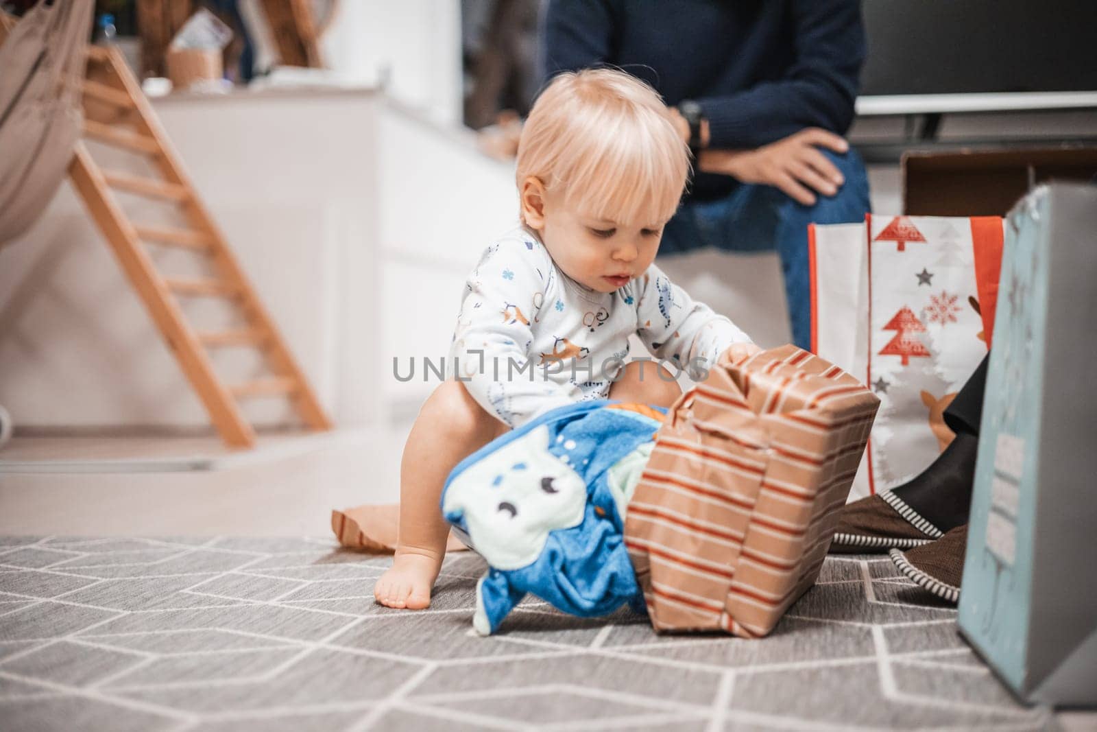 Cute little blond Caucasian toddler unpacking Christmas or Birthday present. Adorable small infant baby boy opening gift by kasto