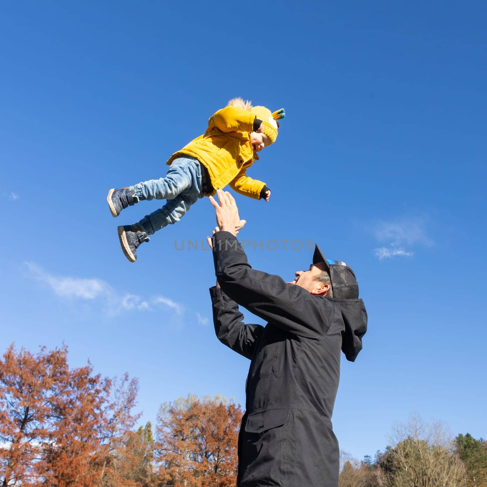 More, more,...dad, that's fun. Happy young father throws his cute little baby boy up in the air. Father's Day, Father and his son baby boy playing and hugging outdoors in nature in fall. by kasto