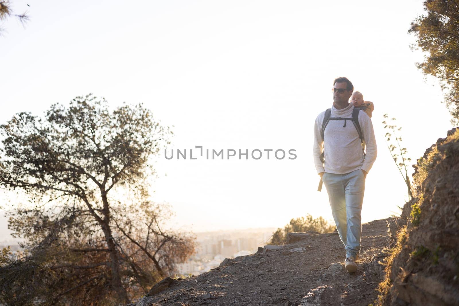 Young father carrying his infant baby boy son in backpack while tracking around Malaga, Spain in sunset. Family travel and vacation concept by kasto