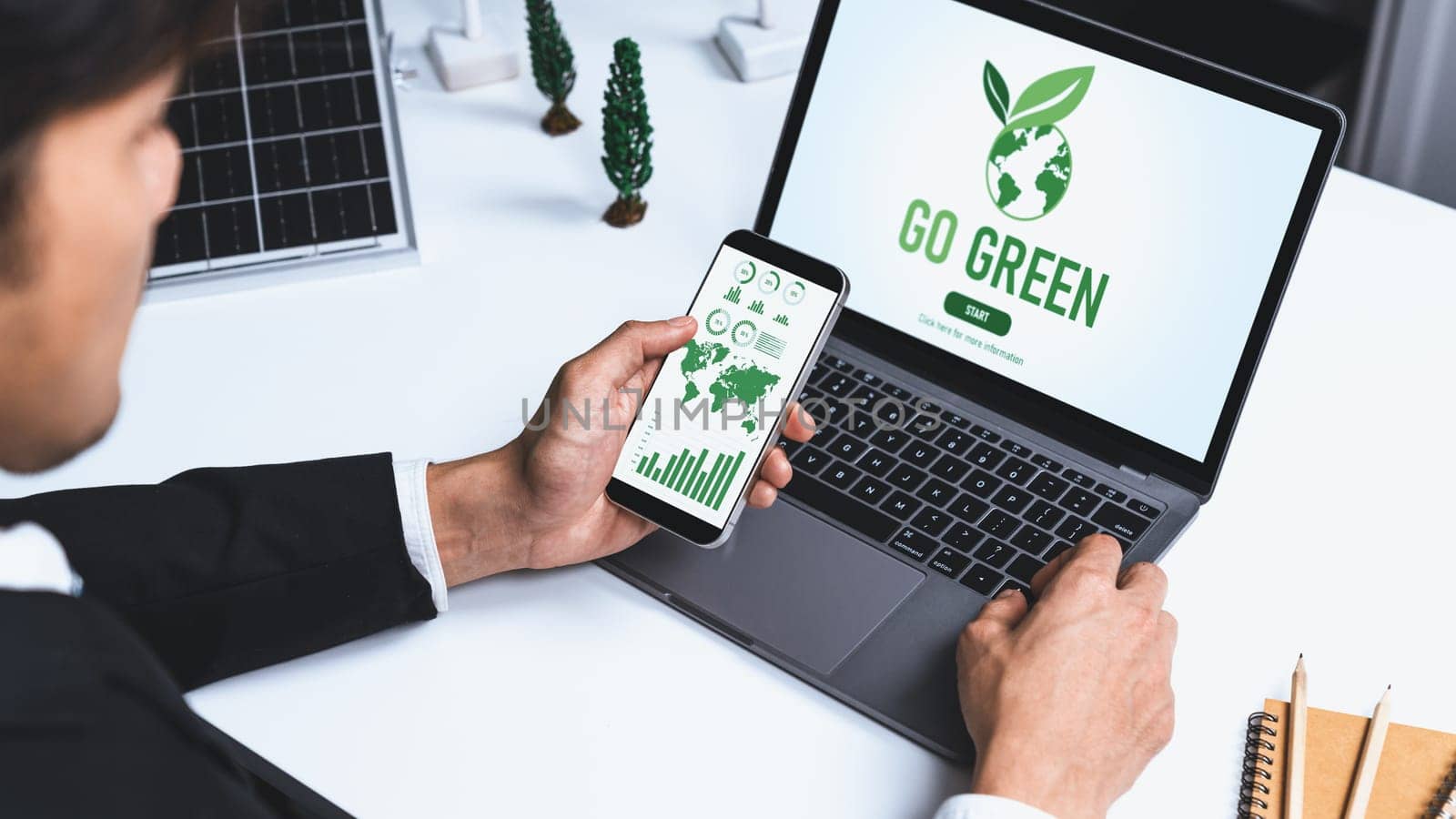 Businessman working in office developing plan or project on eco-friendly alternative energy with solar cell technology display on computer screen for greener environment as apart of CSR effort. Gyre