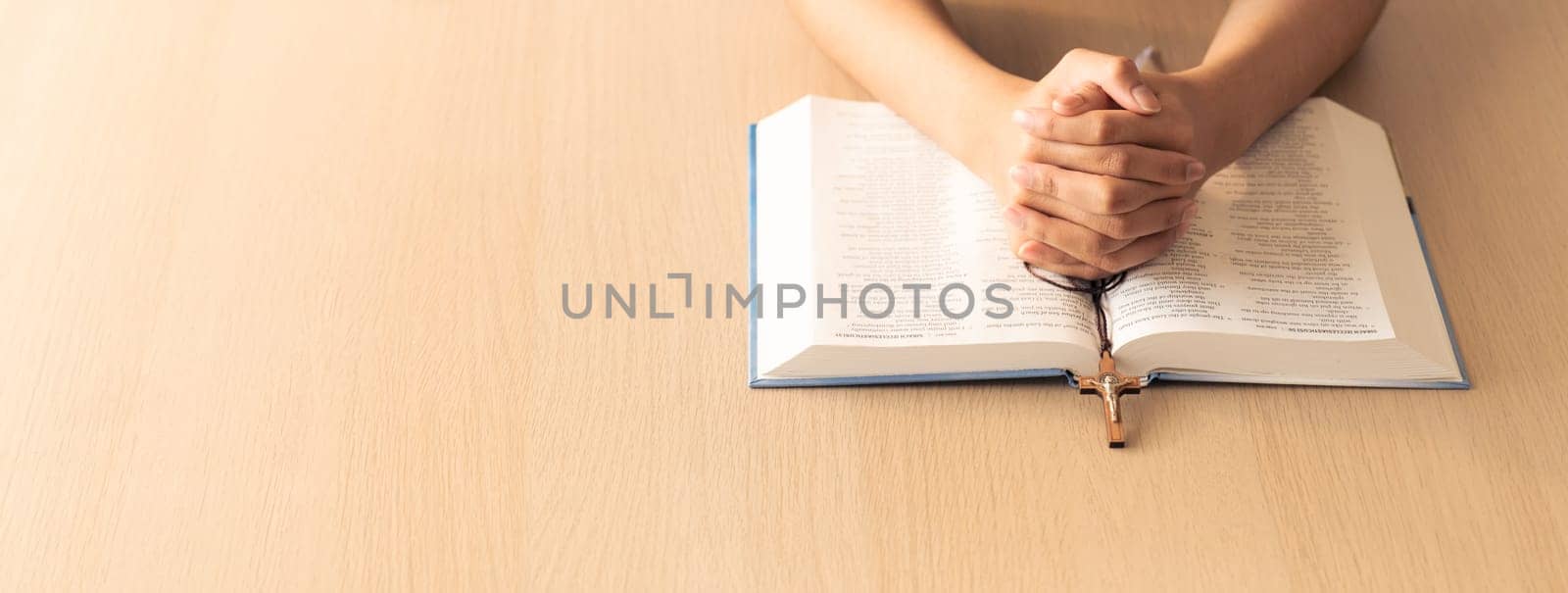 Cropped image of praying male hand holding cross on holy bible book at wooden table. Top view. Concept of hope, religion, faith, christianity and god blessing. Warm and brown background Burgeoning.