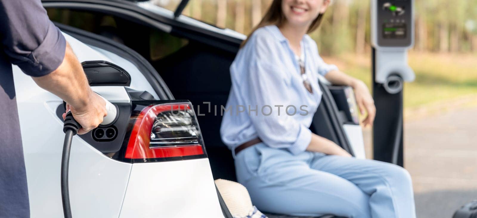 Lovely young couple recharging battery for electric car in autumn. Exalt by biancoblue