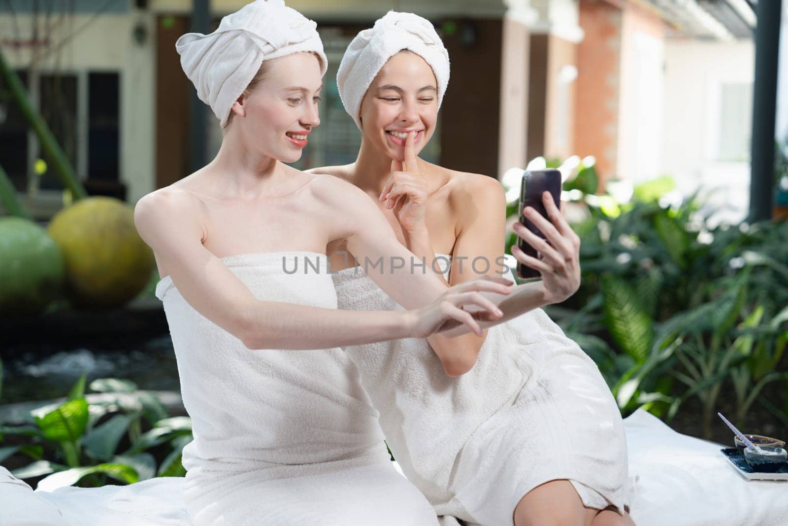 Couple of young beautiful women with beautiful skin in white towel taking a photo together at outdoor surrounded by peaceful natural environment. Beauty and healthy spa concept. Tranquility.