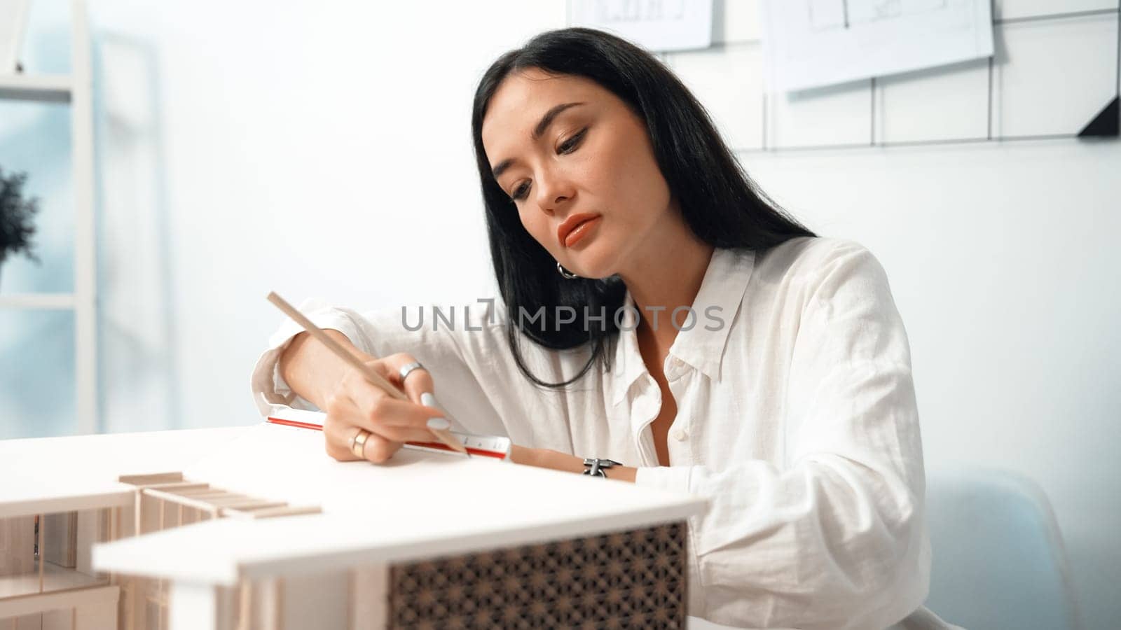 Closeup portrait image of professional young beautiful engineer architect using triangular scale measures house model with focusing at modern office. Business creative design concept. Immaculate.