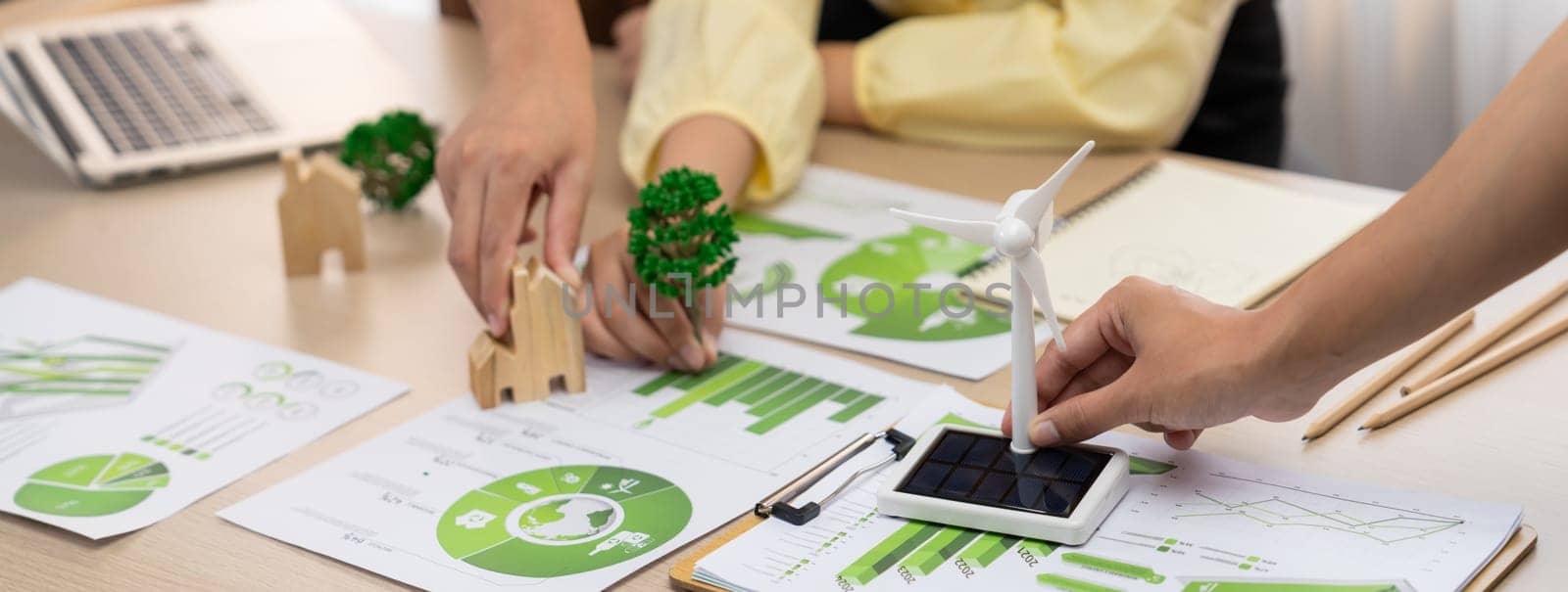 Windmill model represented using renewable energy placed during presenting green business on table with wooden block and environmental document scatter around. Closeup. Delineation.