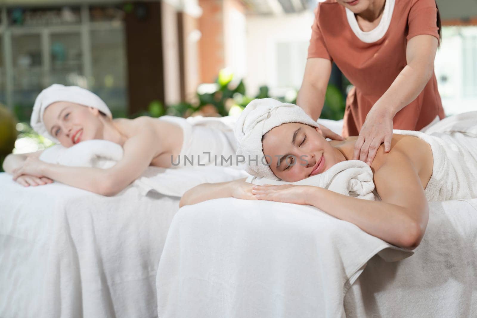 A portrait of two young attractive woman lie on bed during having back massage by a professional masseur at outdoor surrounded by peaceful natural environment. Healthy and beauty concept. Tranquility.