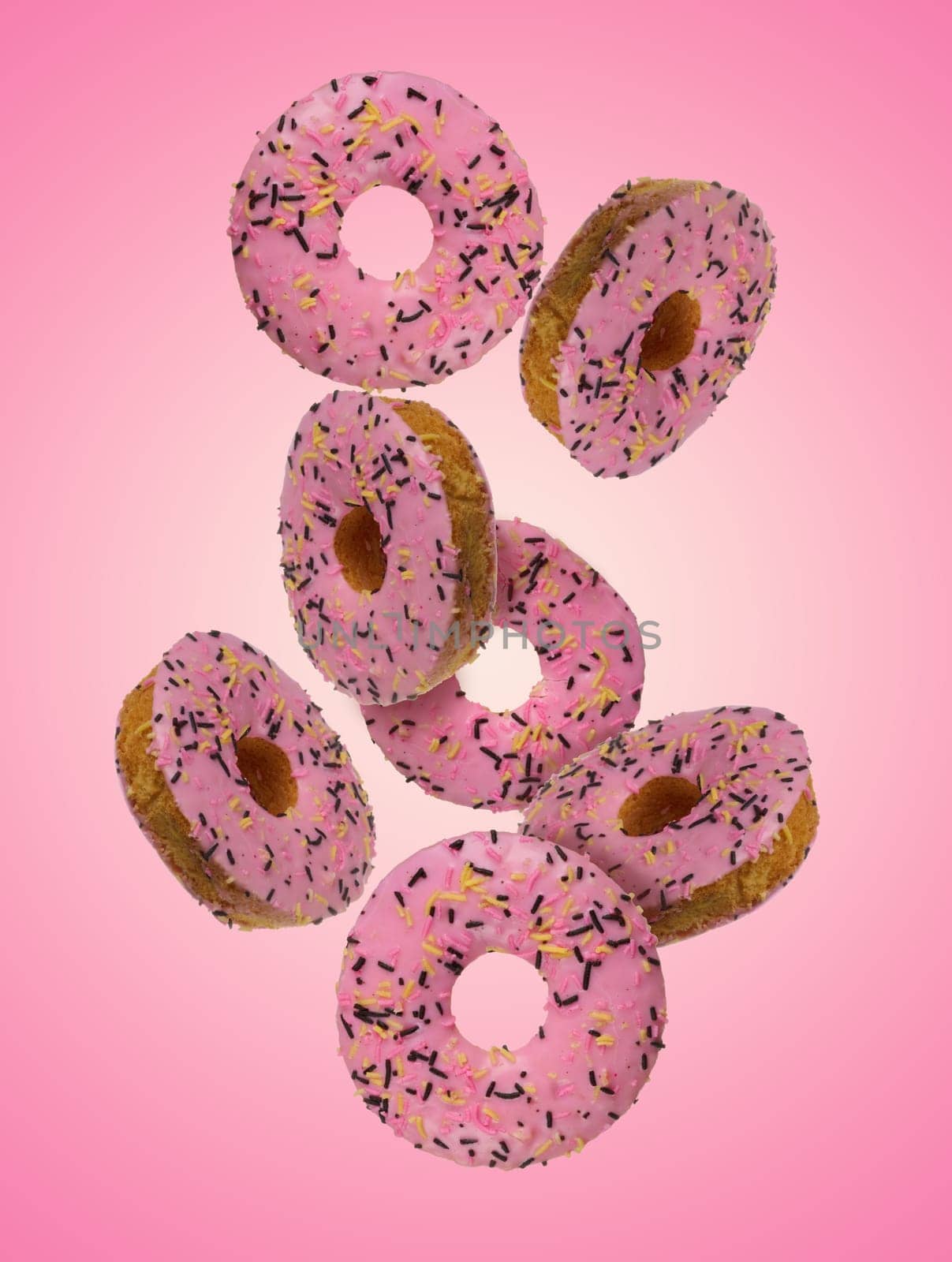 Donuts with pink glaze and sprinkled with colorful sprinkles levitate on a pink background