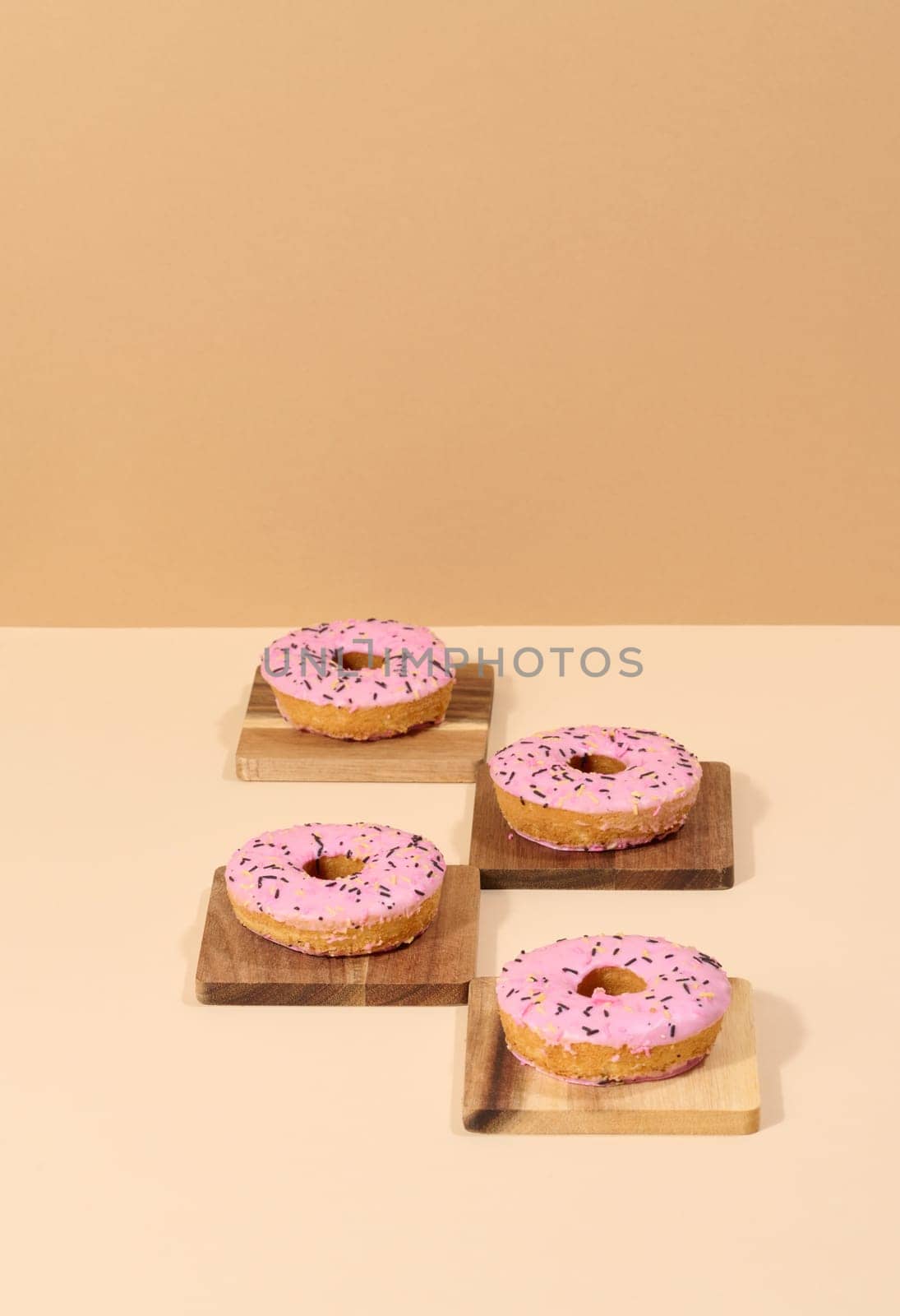 Donut covered with pink glaze and sprinkled with colorful sprinkles, brown background