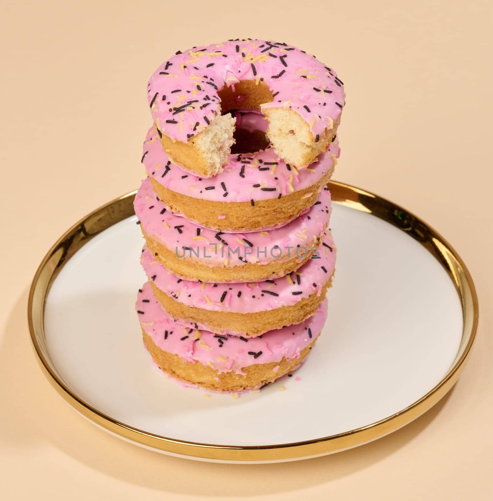 Donut covered with pink glaze and sprinkled with colorful sprinkles on a round plate, brown background by ndanko